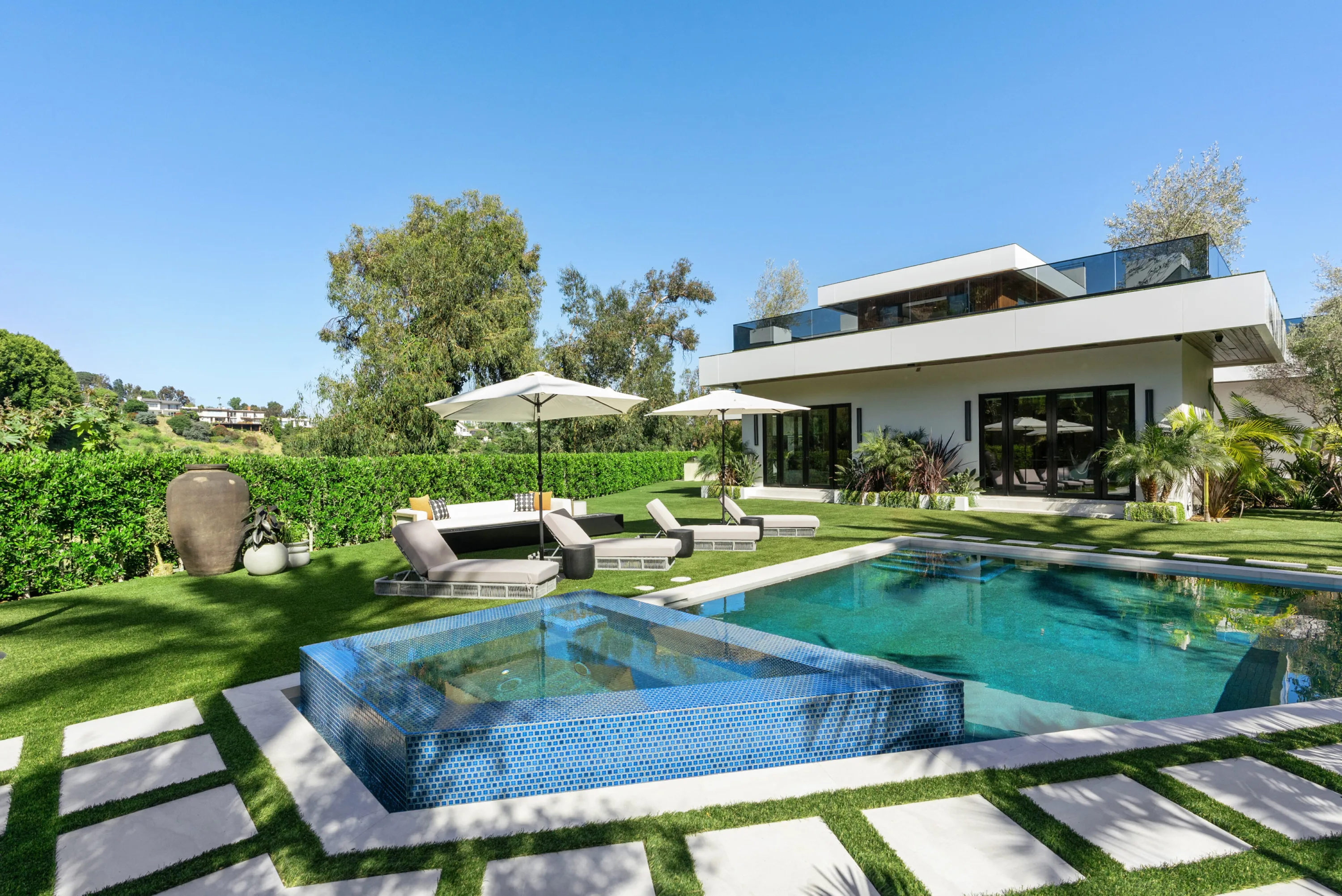 Tiled pool and raised spa on the lawn, with shaded loungers facing the villa's glass rear facade in Bel Air