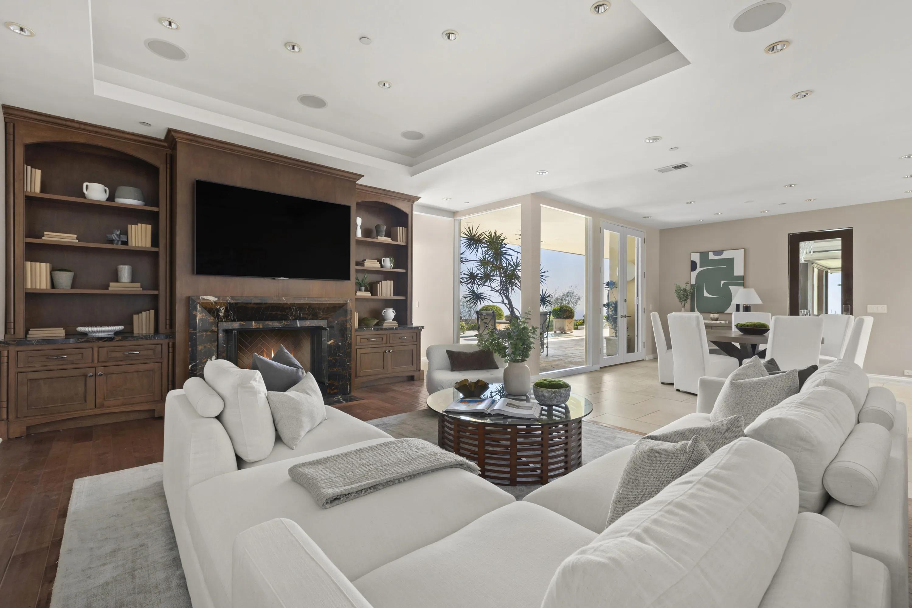 Family room with wall-mounted TV over a marble fireplace, built-in shelving and dining room beyond