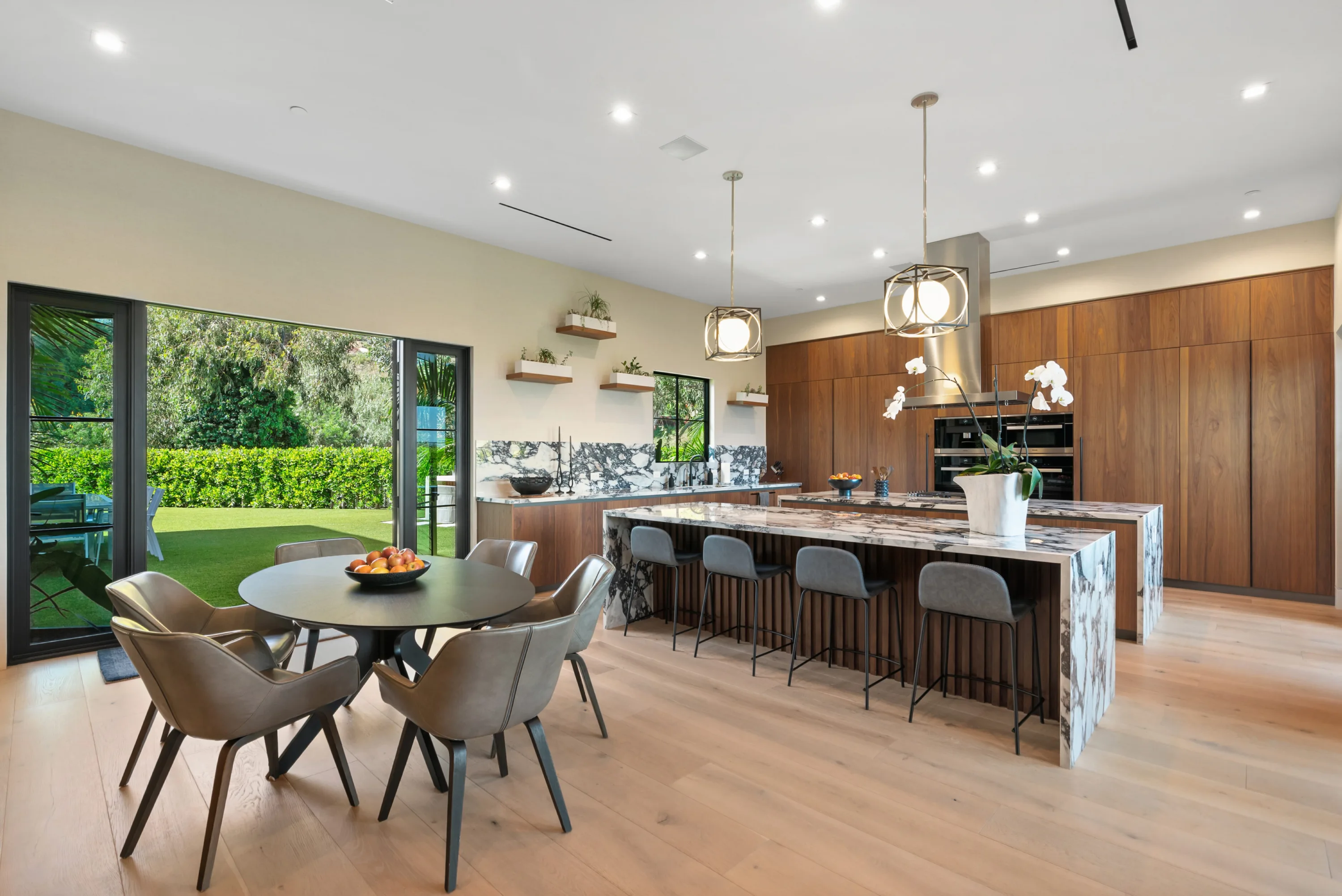 Chef's kitchen with veined marble island, four bar stools and a round breakfast table beside folding glass doors
