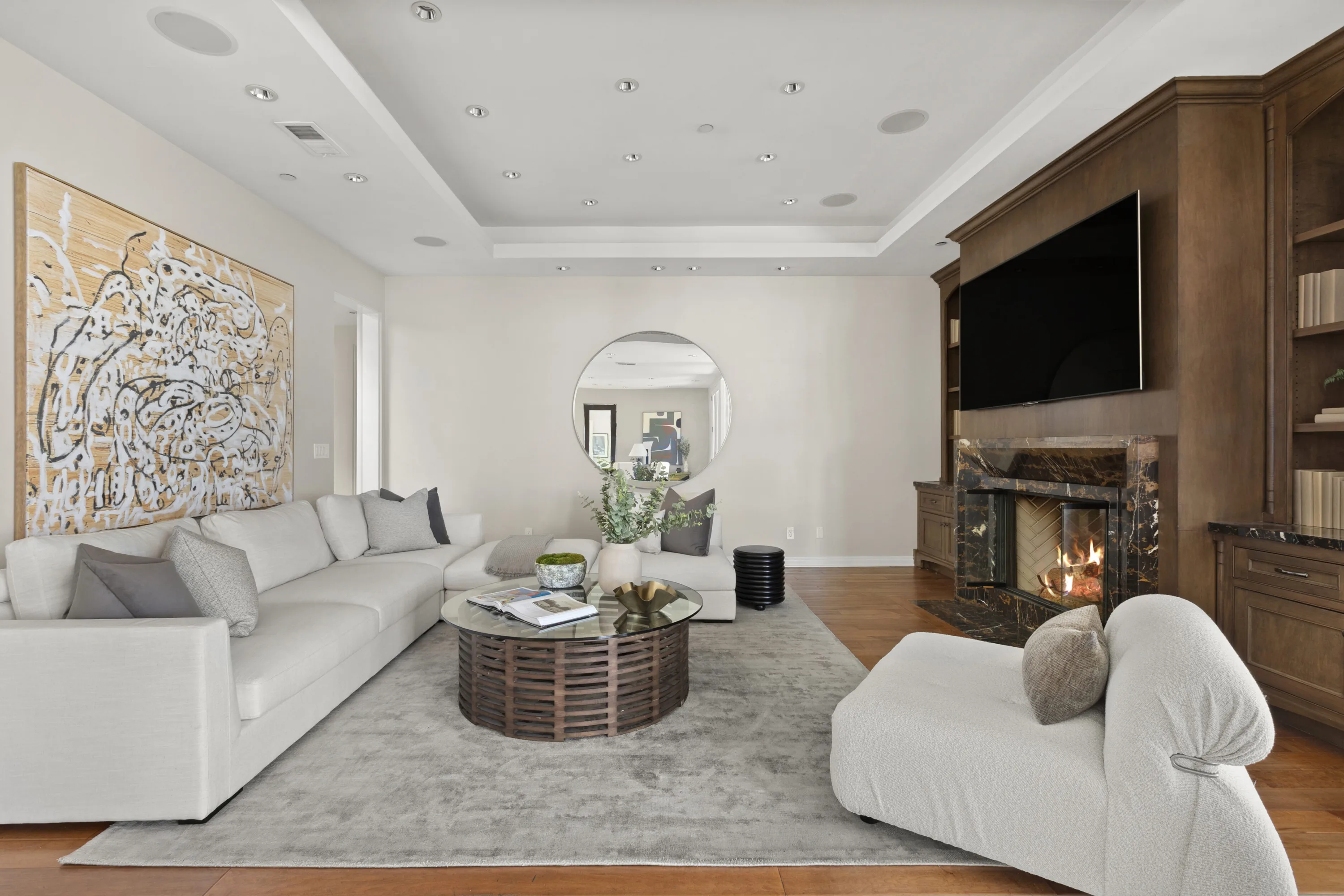 Second sitting room anchored by a large abstract canvas, round mirror and lit fireplace
