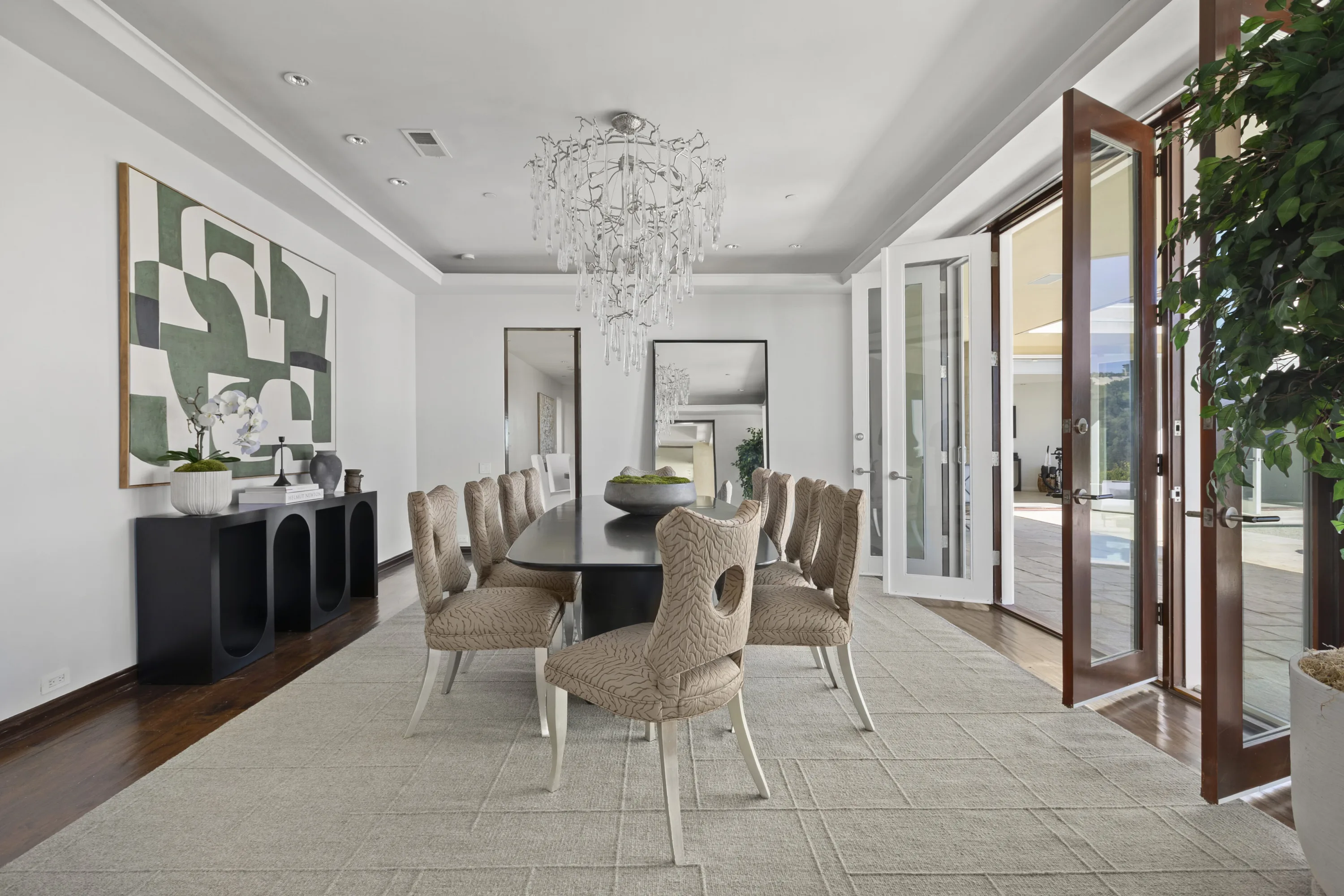 Formal dining room seating ten under a crystal branch chandelier, French doors out to the pool terrace