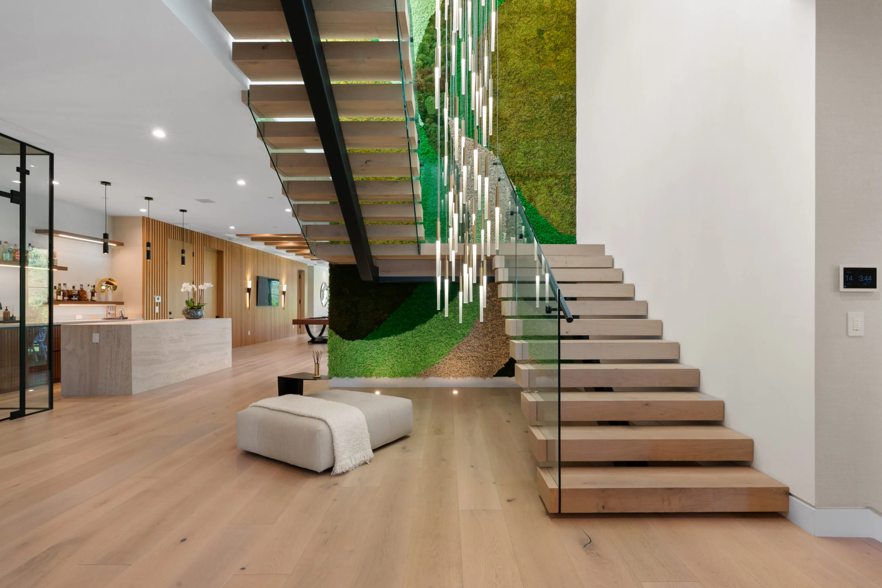 Floating oak staircase against a preserved moss wall, bar counter and entertaining space beyond