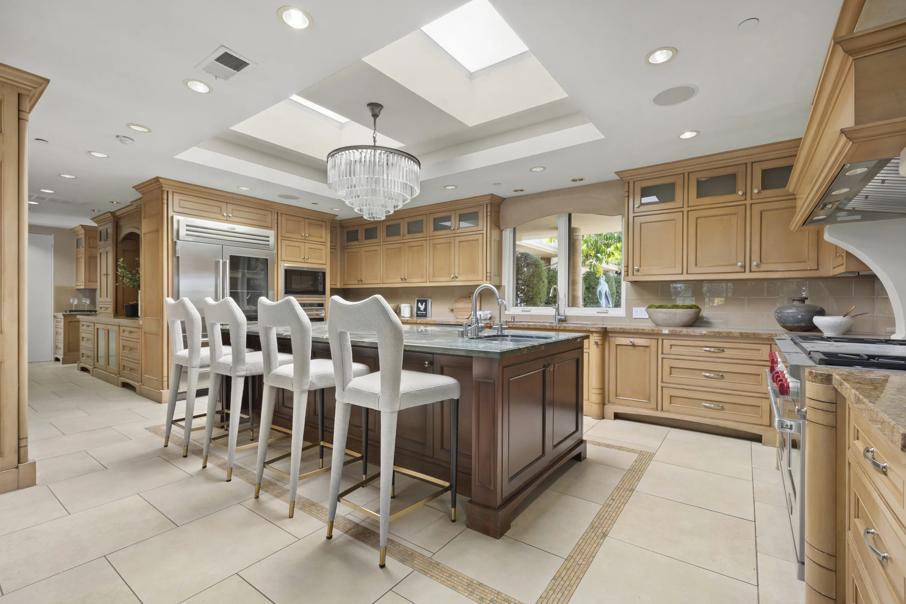 Chef's kitchen with skylit ceiling, green stone island and four upholstered bar stools