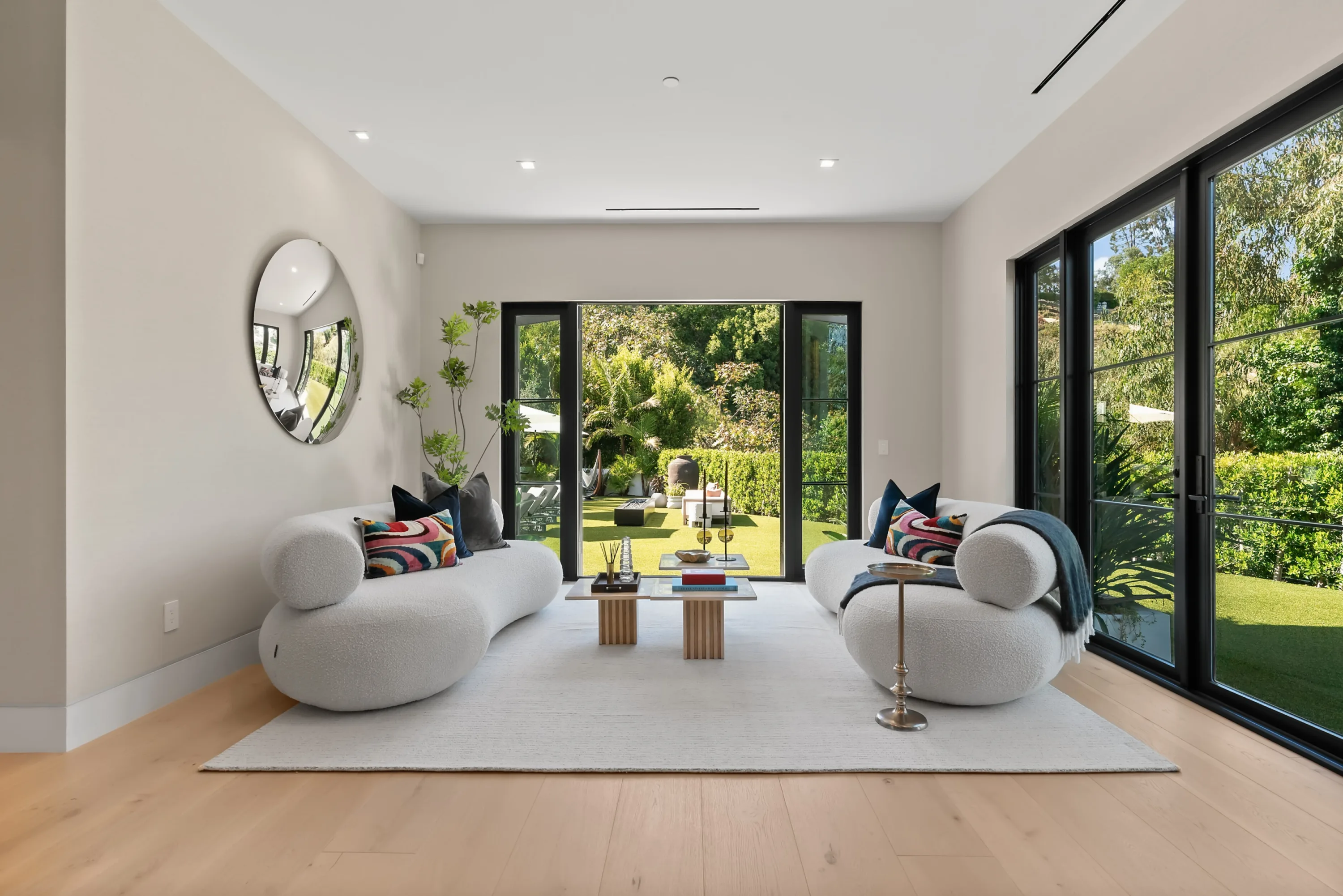 Sitting room with two rounded bouclé sofas framing open doors to the hedged lawn