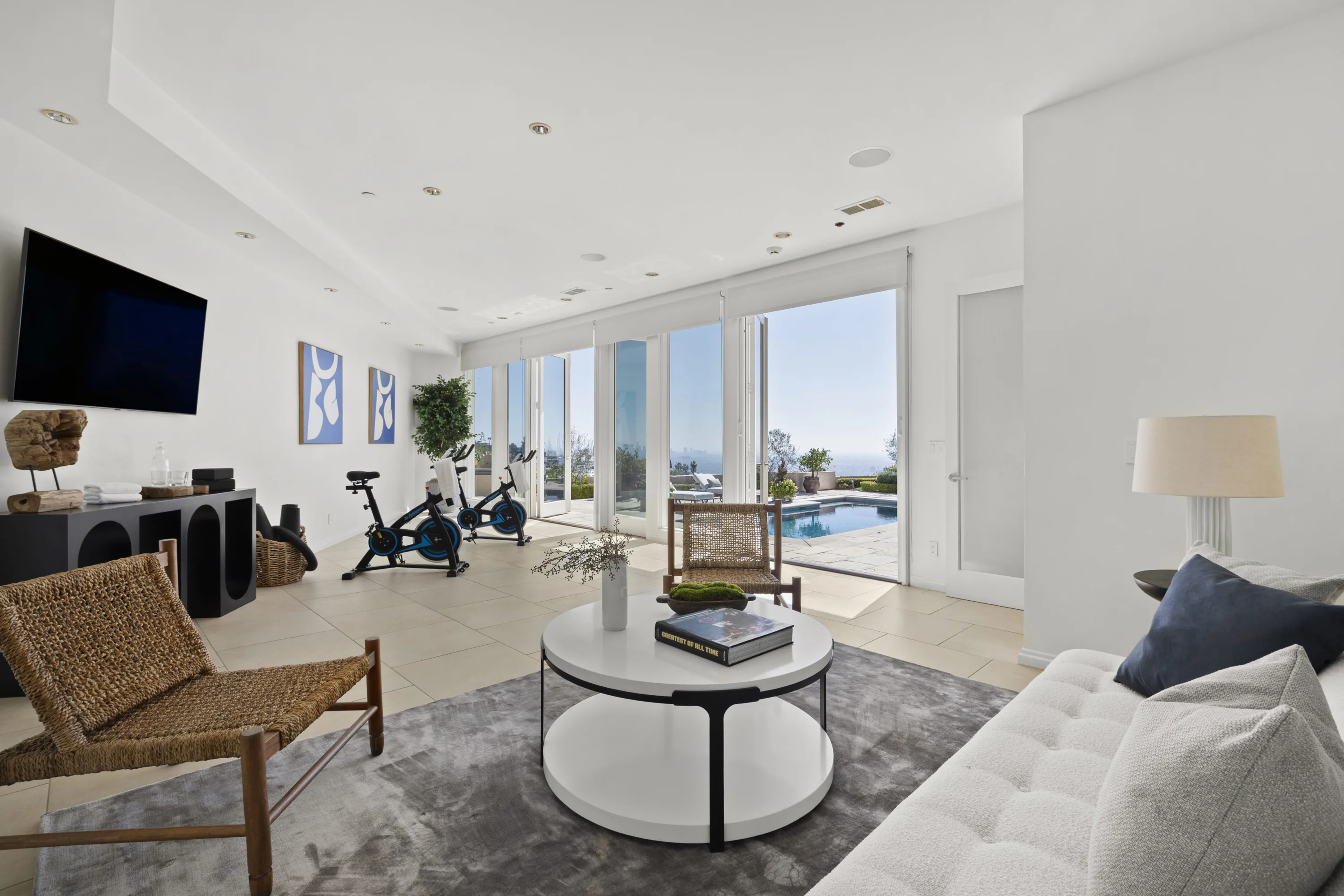 Gym and lounge with two spin bikes, wall TV and sliding doors open to the pool deck