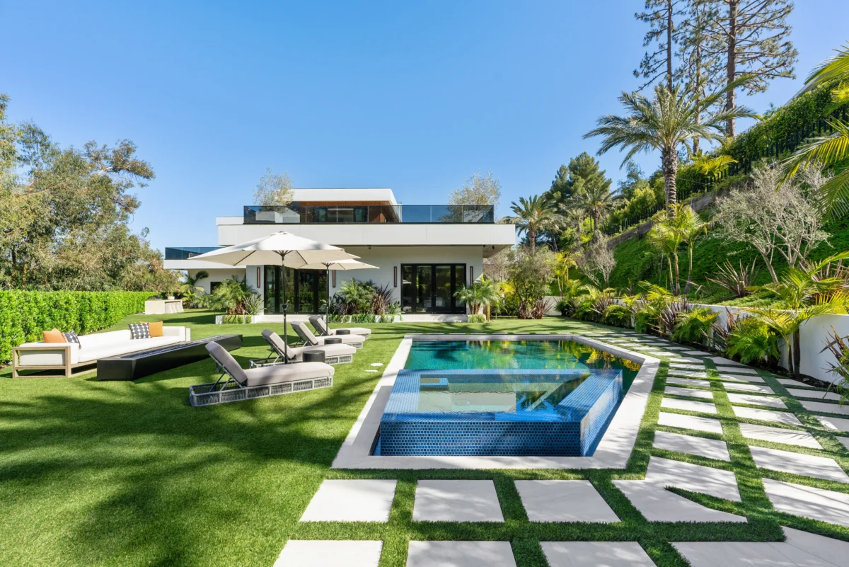 Rear elevation across the lawn, pool and spa in the foreground with rooftop terrace above the glass doors