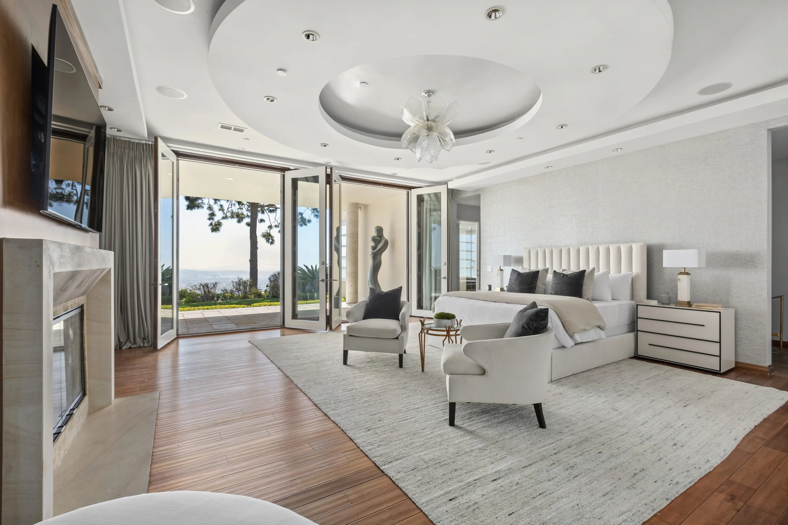 Primary suite under a domed ceiling, fireplace to one side and doors opening to treetops and the view