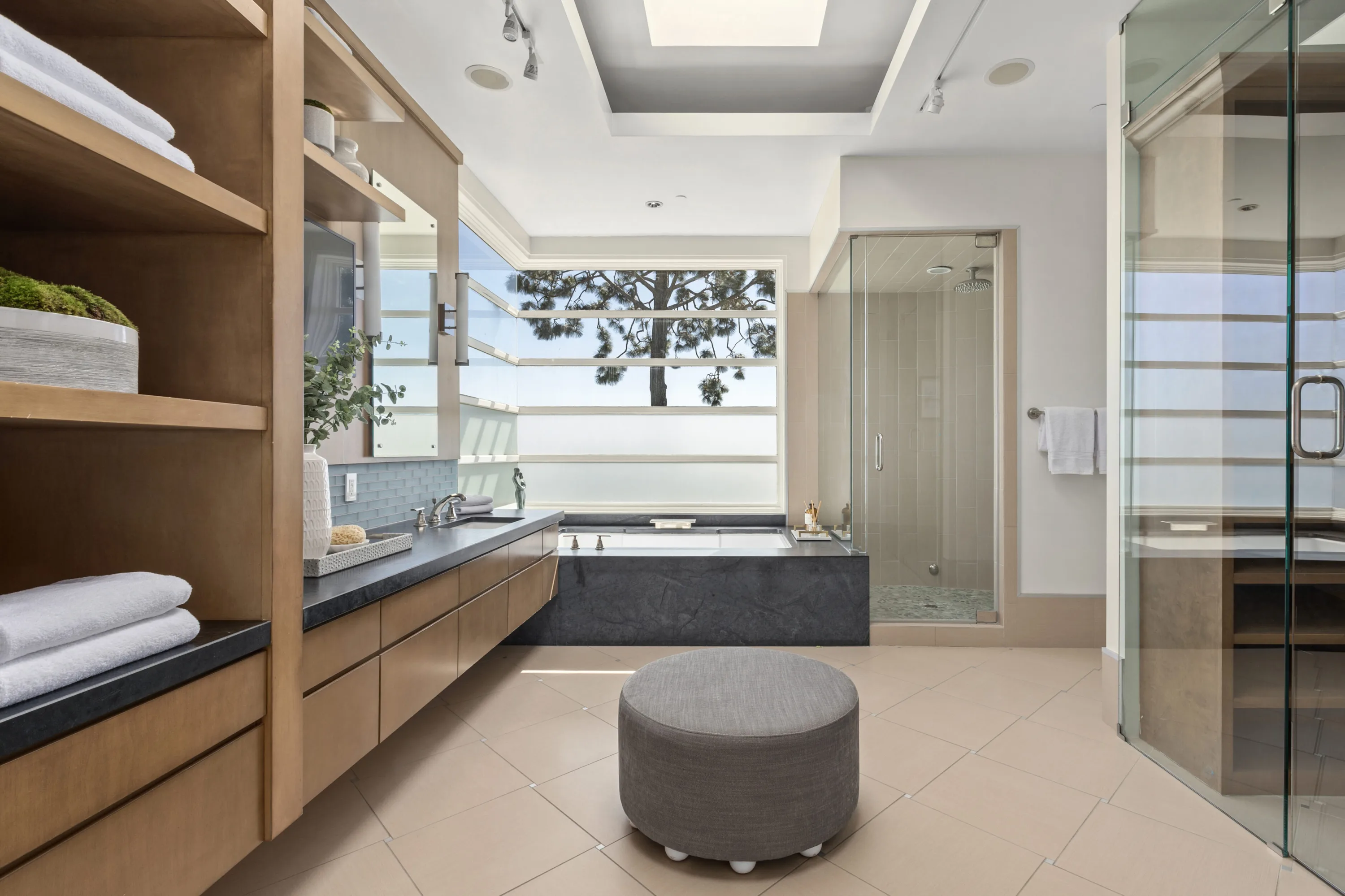 Primary bath with soaking tub below clerestory glass, honed stone vanity, walk-in shower and sauna
