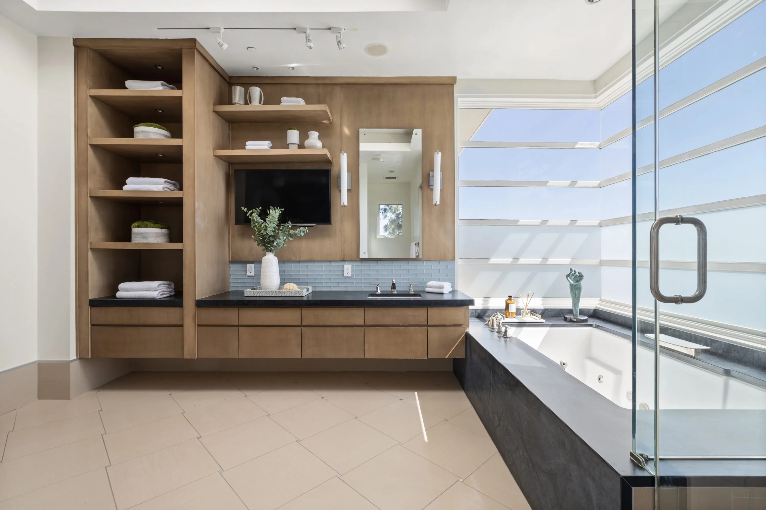 Floating timber vanity with black stone top, wall TV and jetted tub beside louvred windows