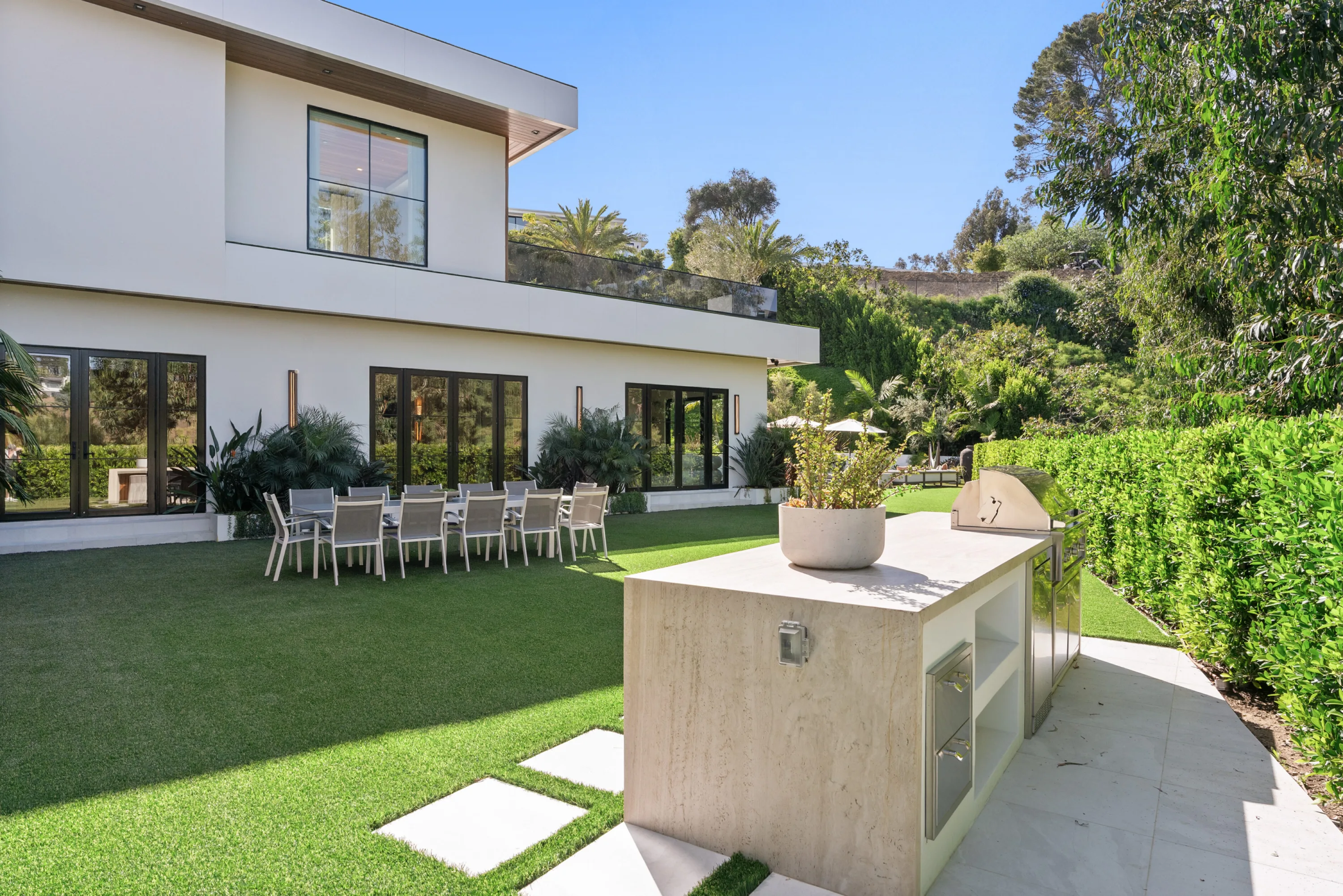 Poolside kitchen island with built-in grill, long alfresco dining table set along the villa's glass wall