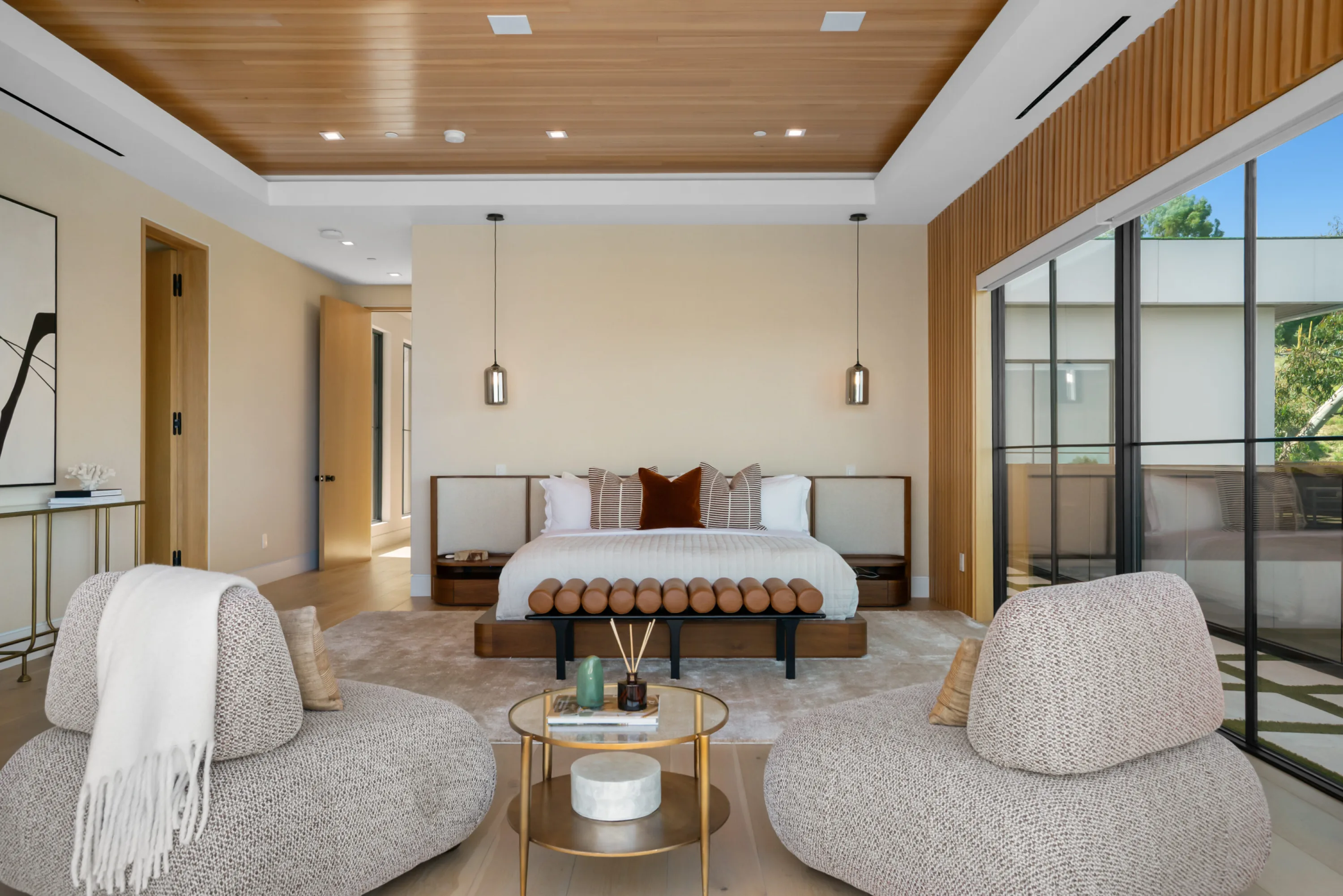Guest suite with upholstered bed, pendant lights and two swivel chairs facing a glazed wall to the terrace