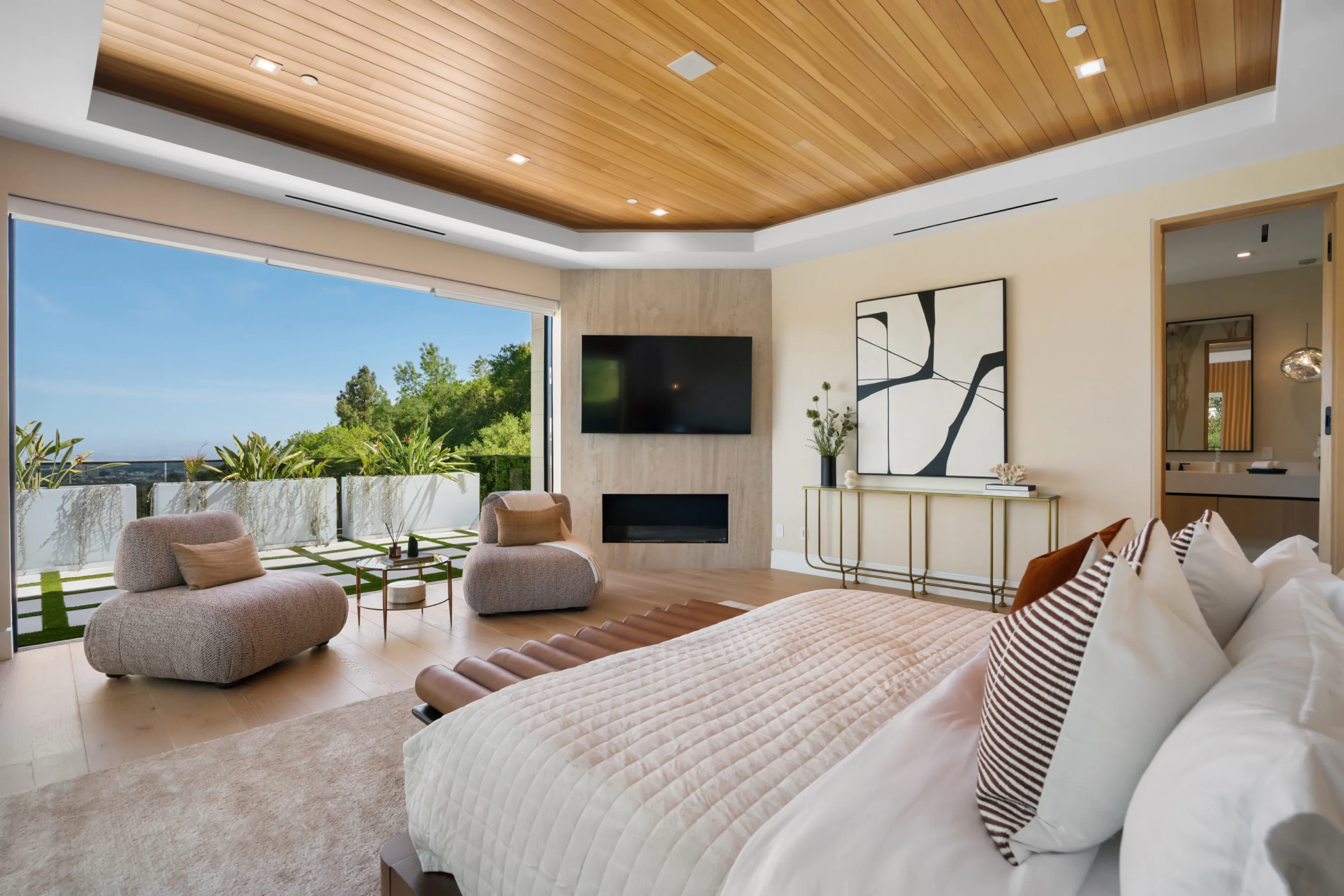 Primary suite with fireplace and TV, lounge chairs beside sliders that open fully to a treetop terrace