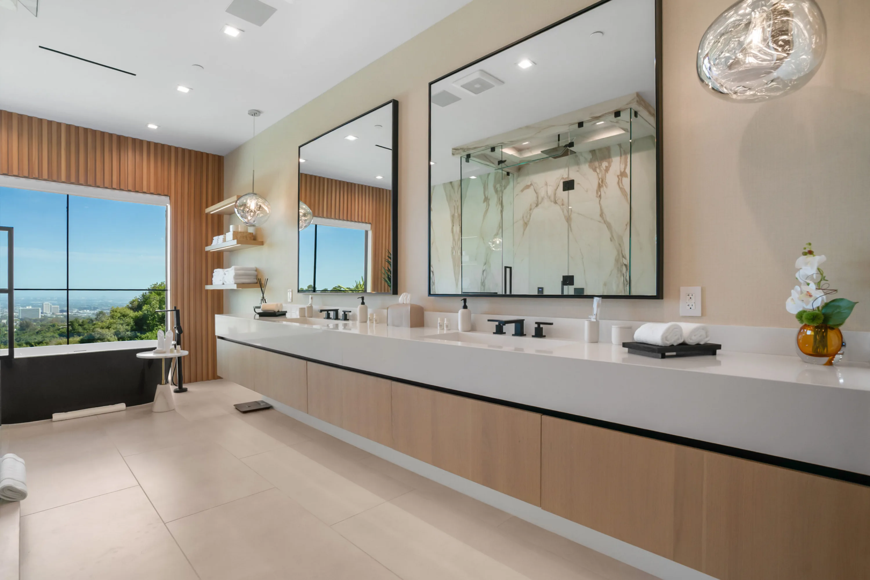 Primary bathroom with long double vanity, twin mirrors and a soaking tub at a window over the city