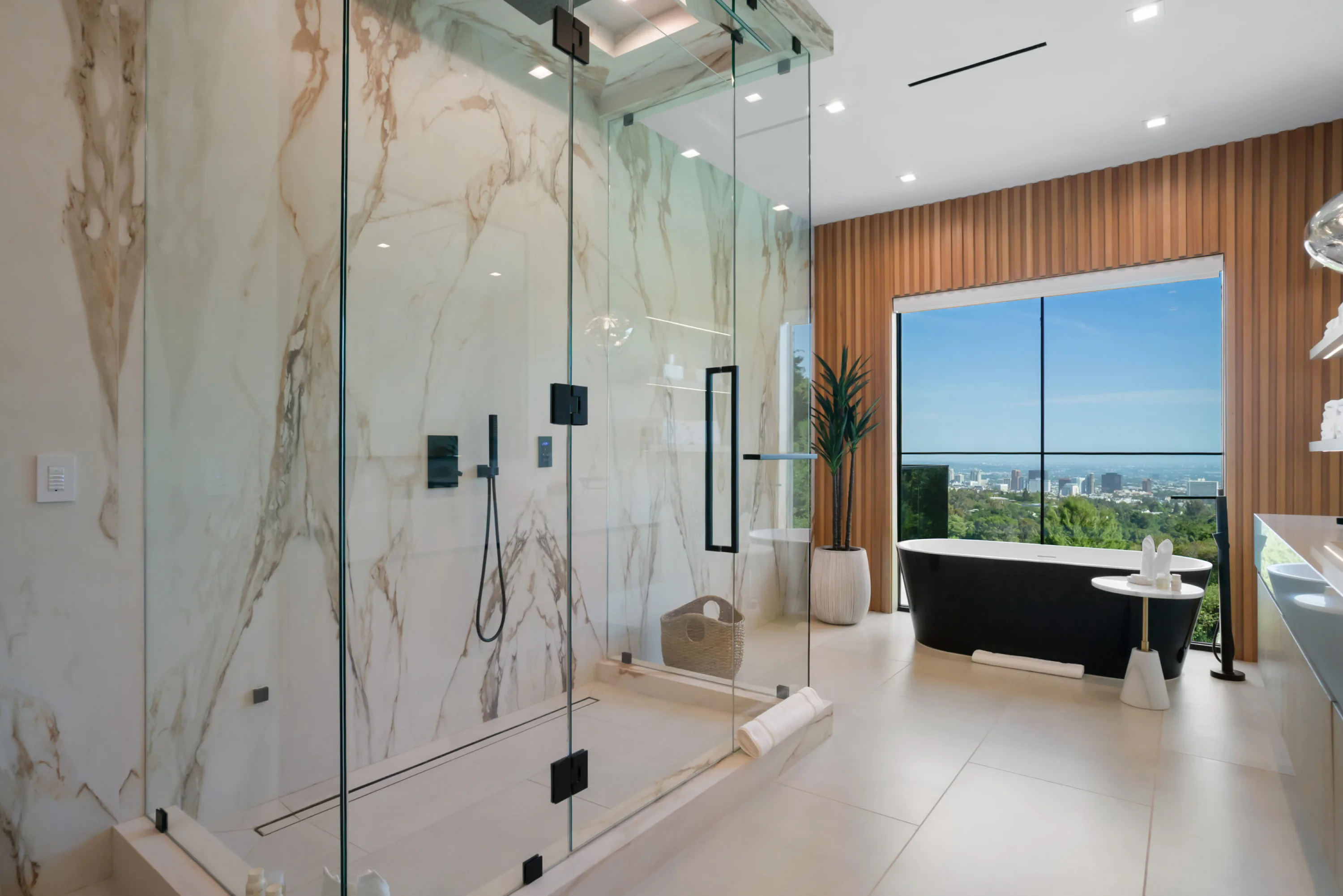 Marble walk-in shower and black freestanding tub framed by a picture window across the basin to downtown