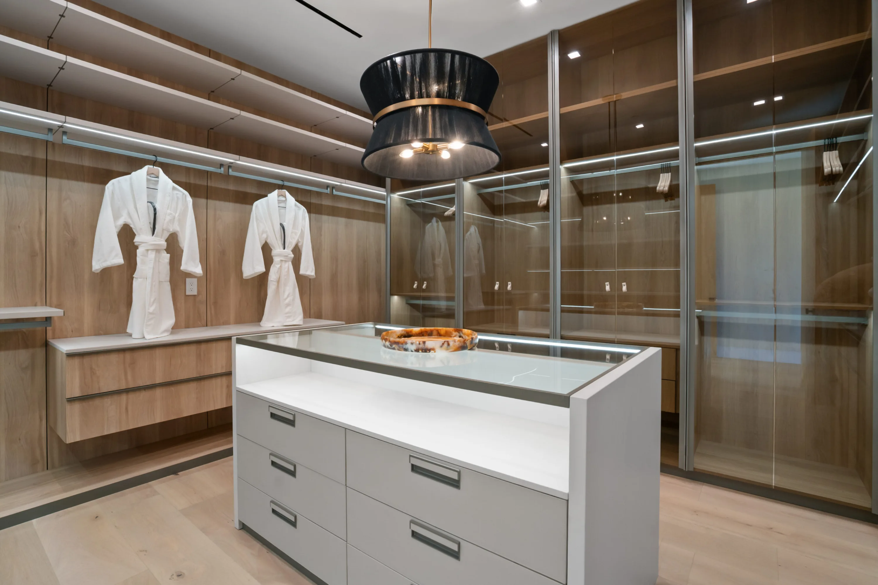 Walk-in dressing room with glass-fronted cabinetry, lit island and two robes hung ready