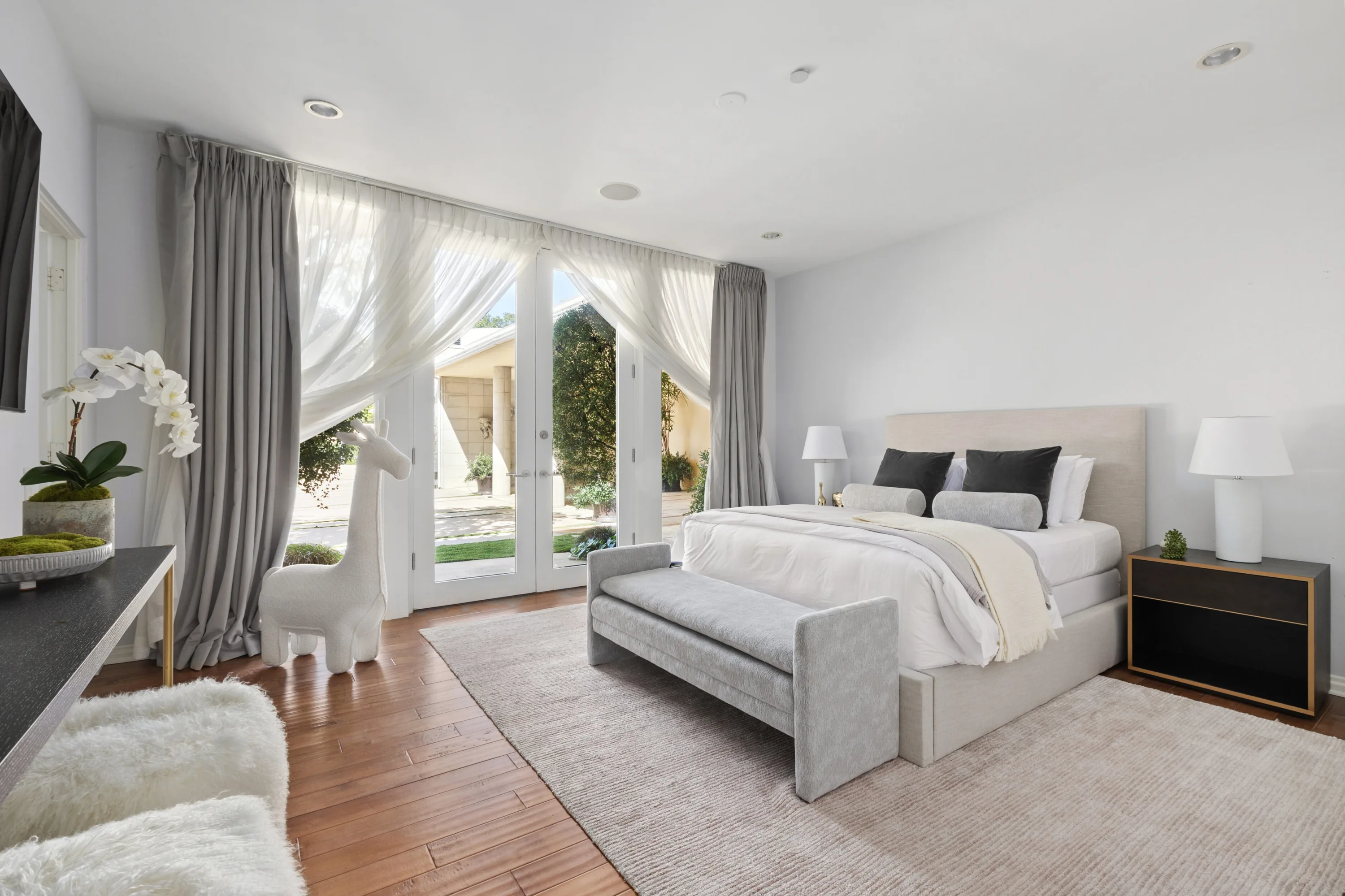 Guest bedroom in soft greys, king bed with upholstered bench and sheer-draped doors to the courtyard