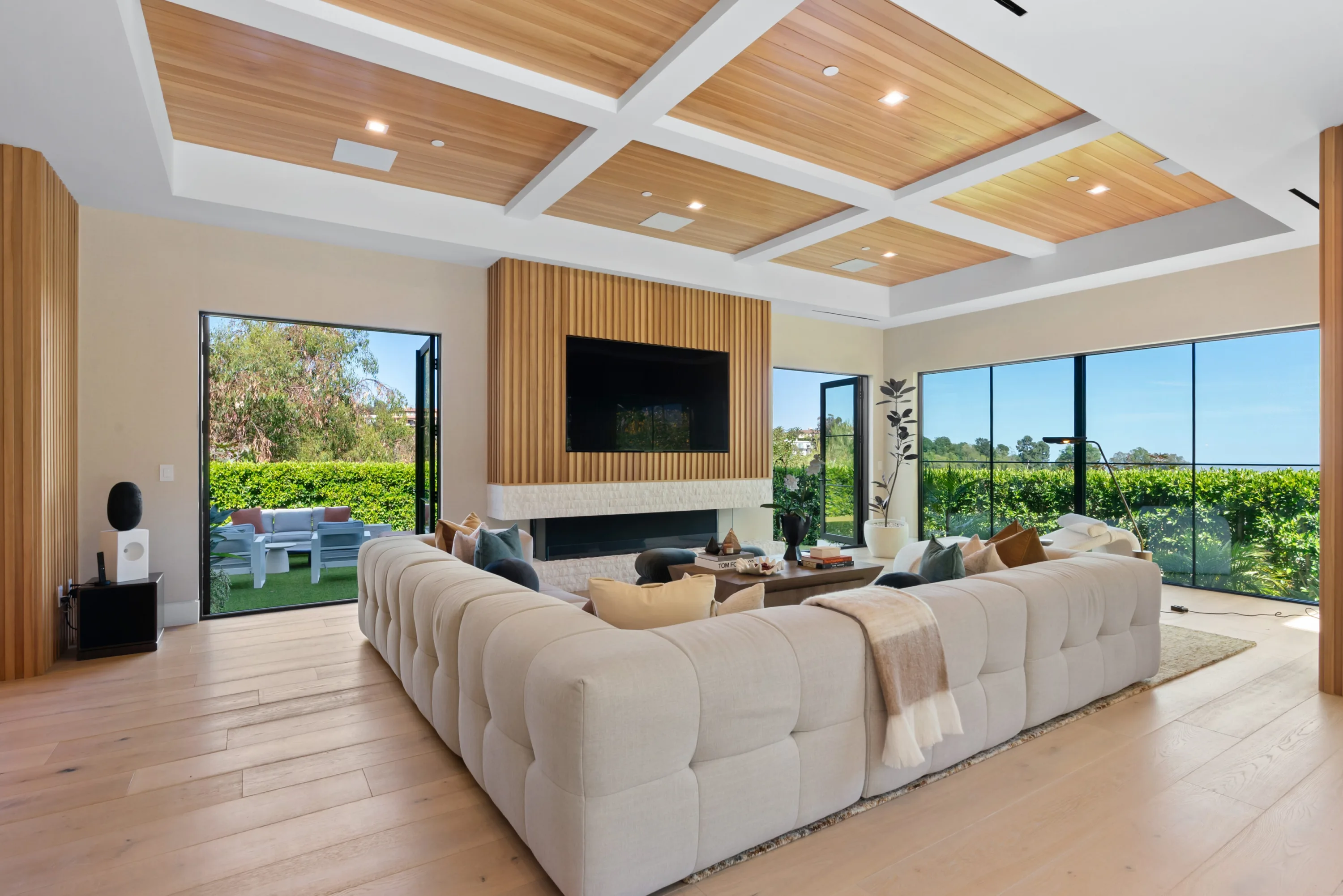 Family lounge with deep tufted sectional, linear fireplace below a wall-mounted TV and sliders open to the lawn