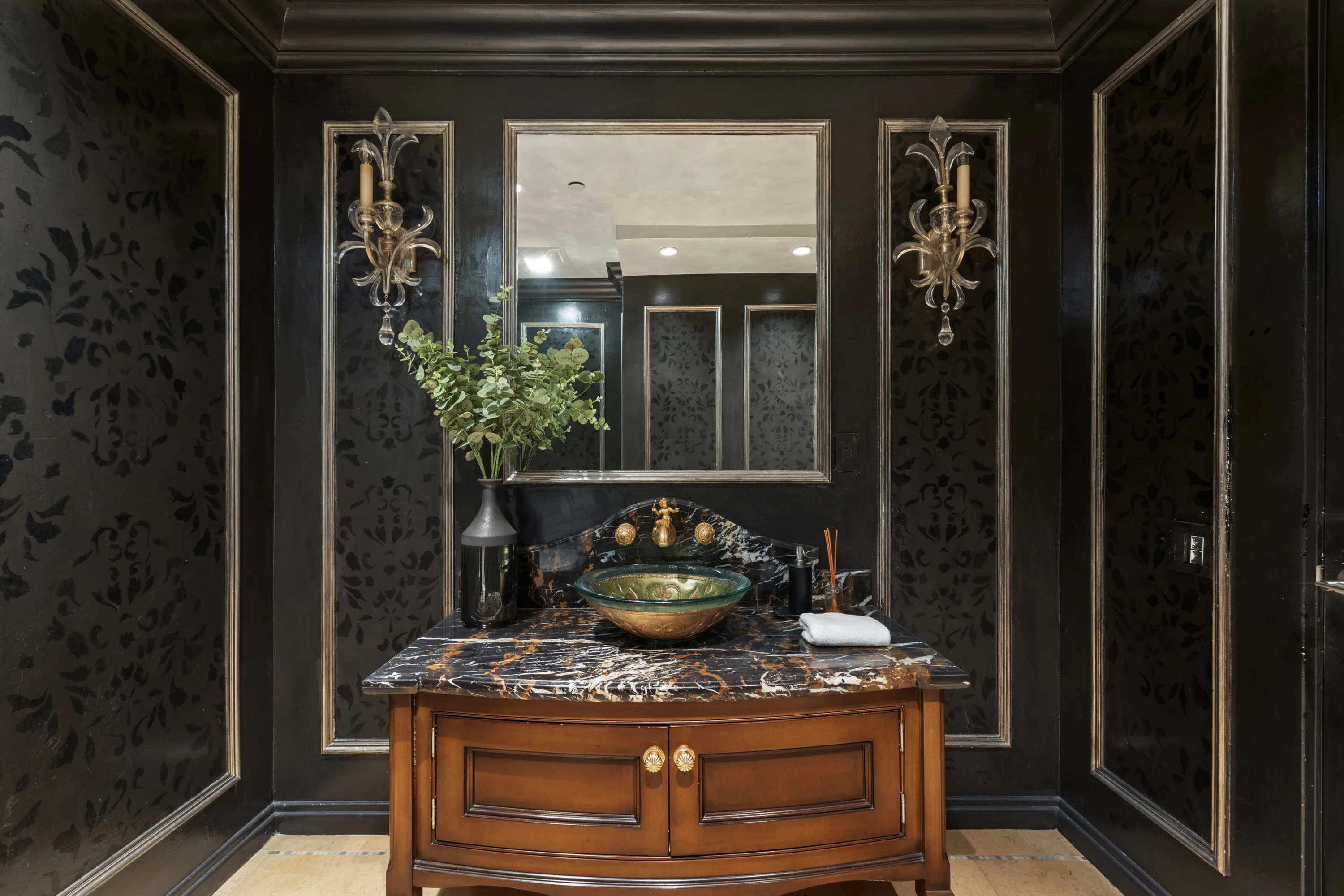 Powder room in black damask panelling with gilt glass basin, marble top and crystal sconces