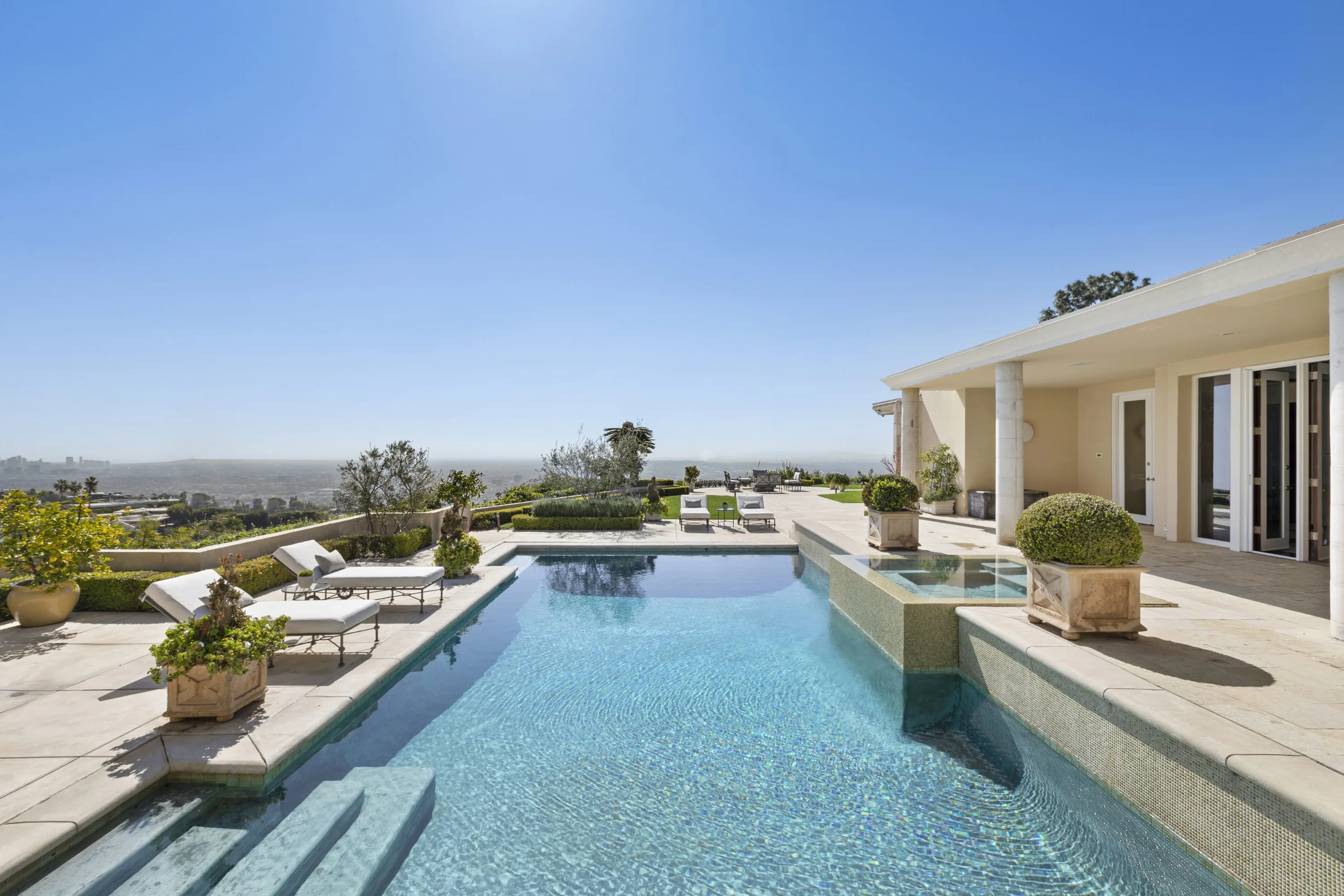 Resort pool and spa on the stone terrace, sun loungers and olive trees above the city haze