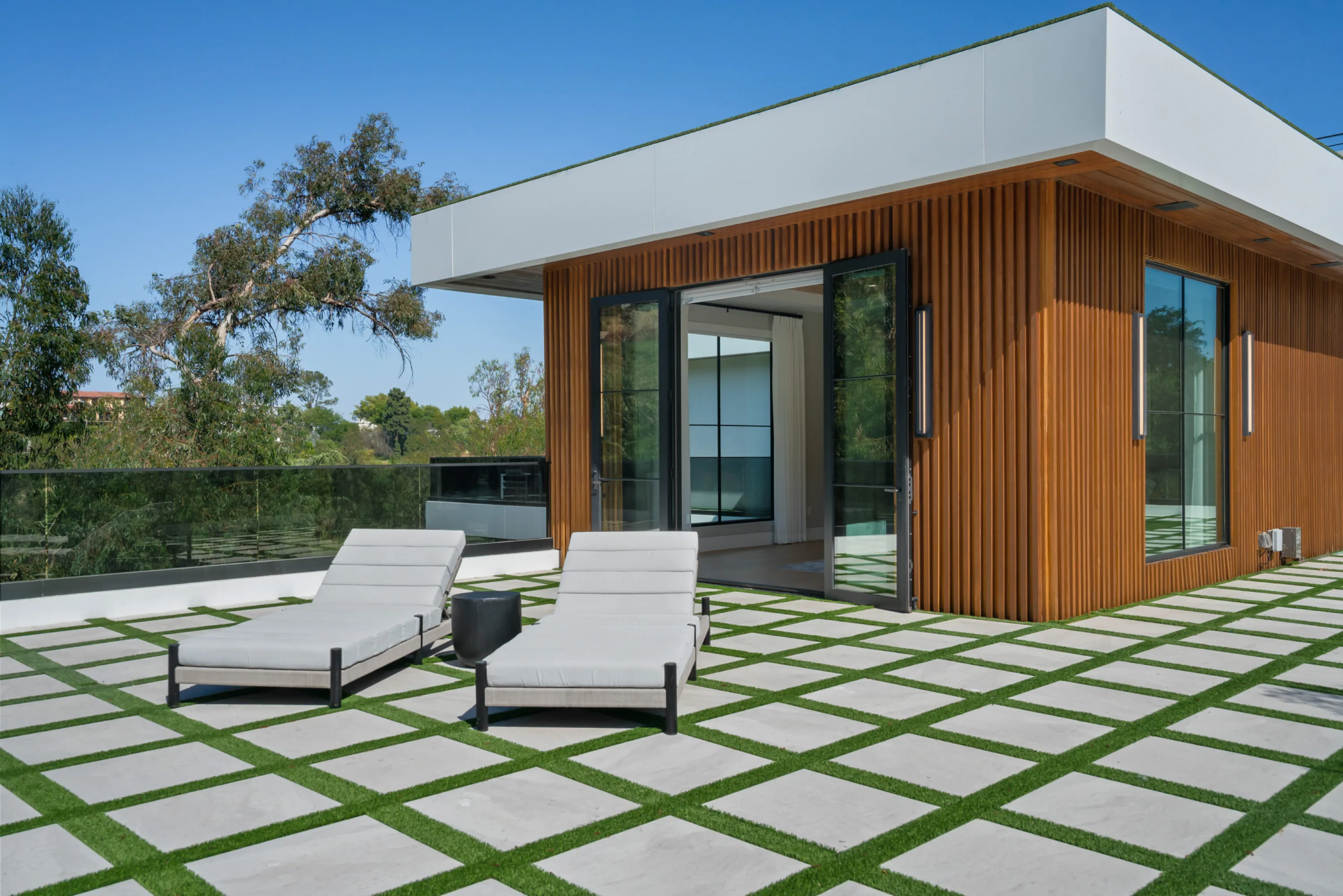 Rooftop terrace paved in grass-jointed stone, two sun loungers outside a cedar-clad lounge