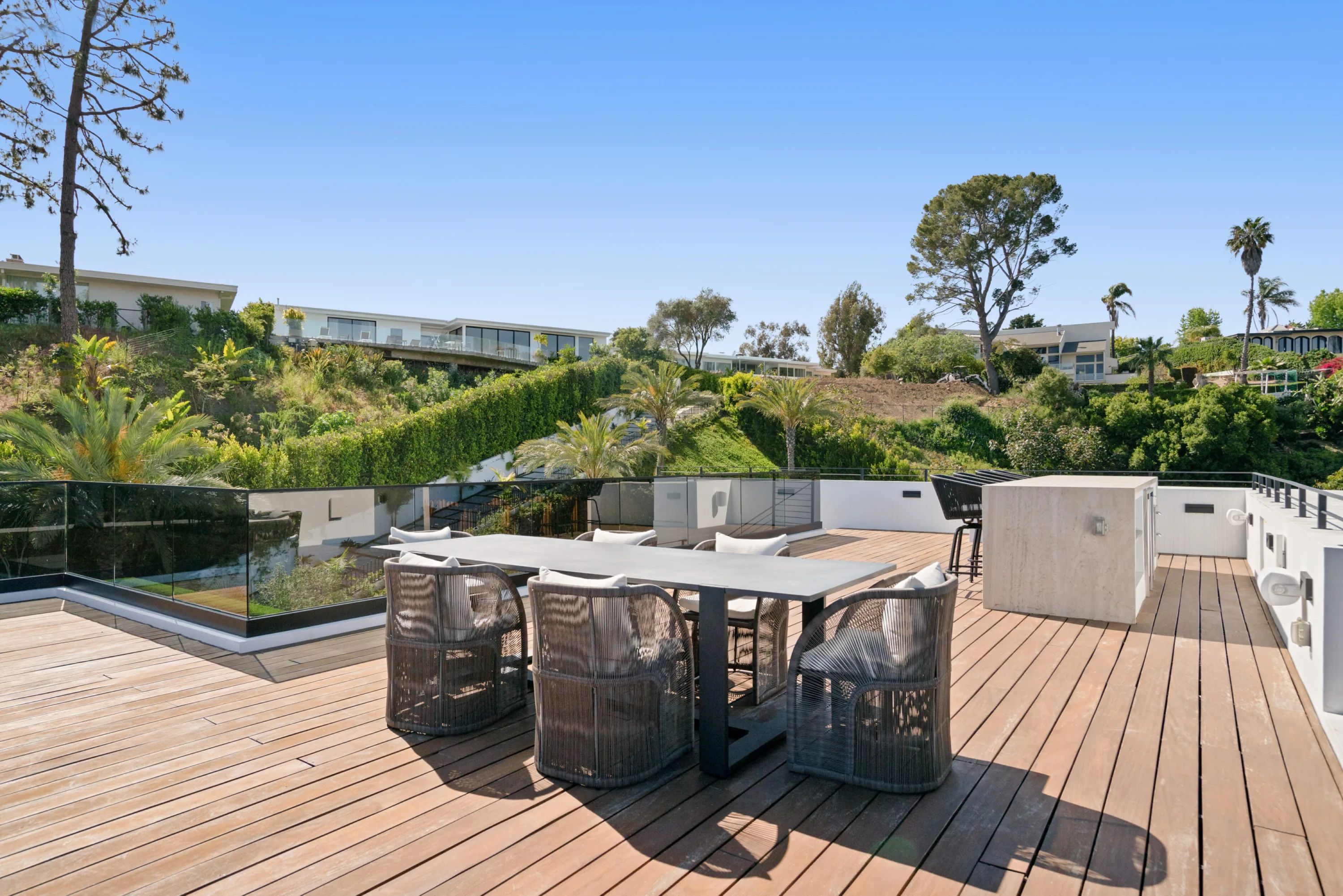 Rooftop deck with long stone dining table, woven chairs and built-in grill above the Bel Air hillside