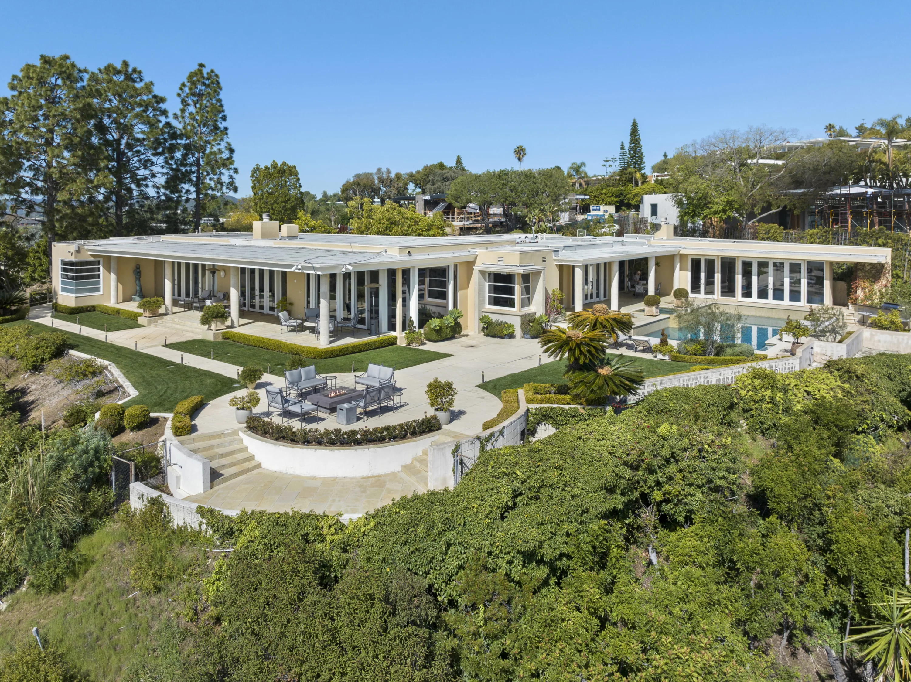 Rear elevation from above: colonnaded terraces, fire-pit seating circle, lawns and pool on the hillside edge