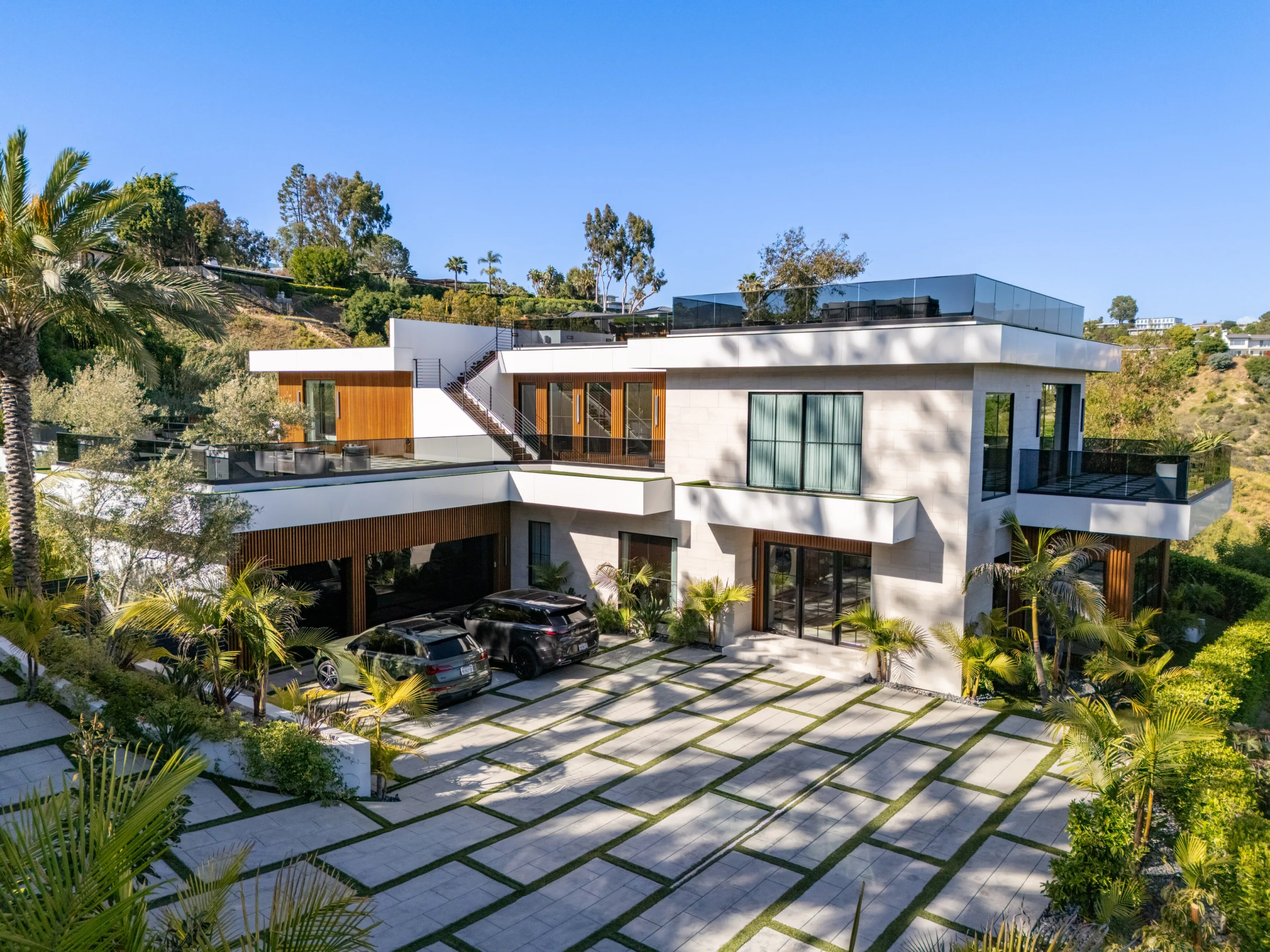 Front elevation with wide paver-and-grass driveway, garage bays and stair to the upper roof terrace