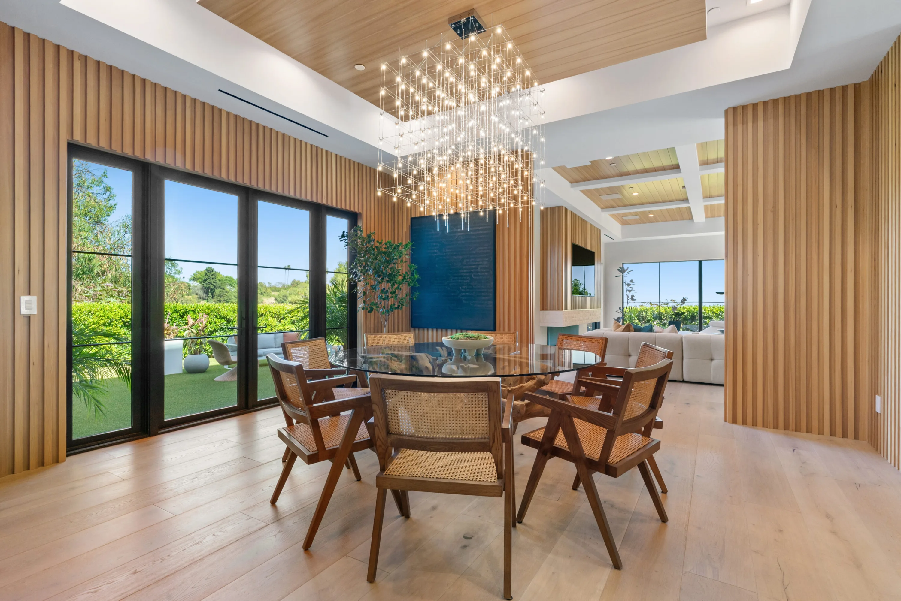 Dining area seating six beneath a cascading crystal chandelier, slatted oak walls and garden doors alongside