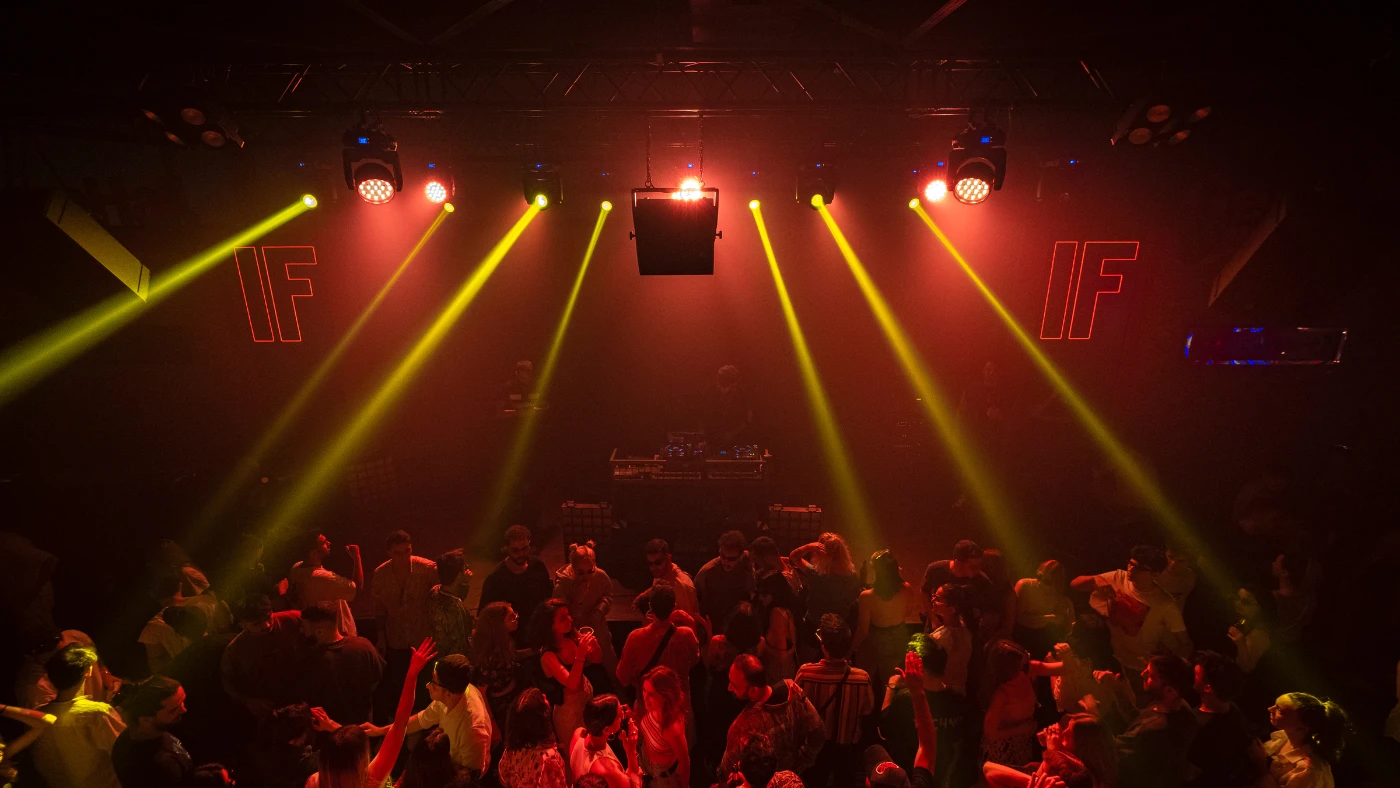 Crowd dancing at a private event under dramatic red and yellow stage lighting.