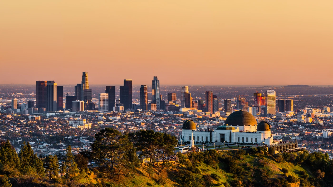 Panoramic Los Angeles skyline at sunset with Griffith Observatory in the foreground.
