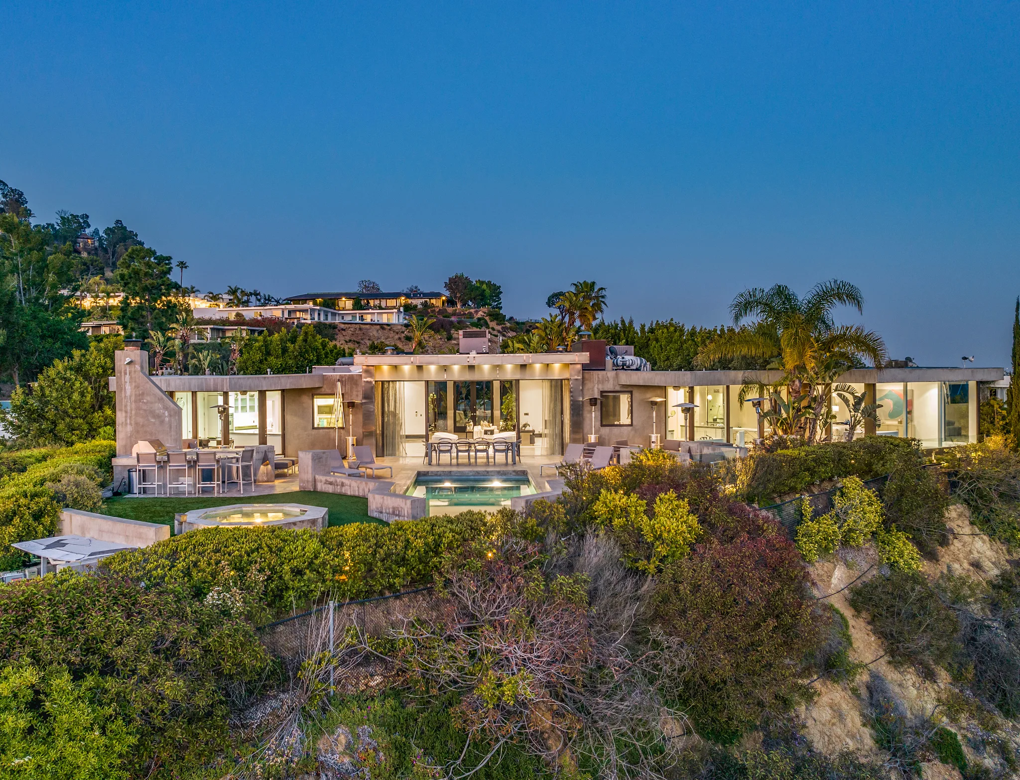 Single-storey Beverly Hills villa lit at dusk, pool, spa and terrace set above a hillside of chaparral