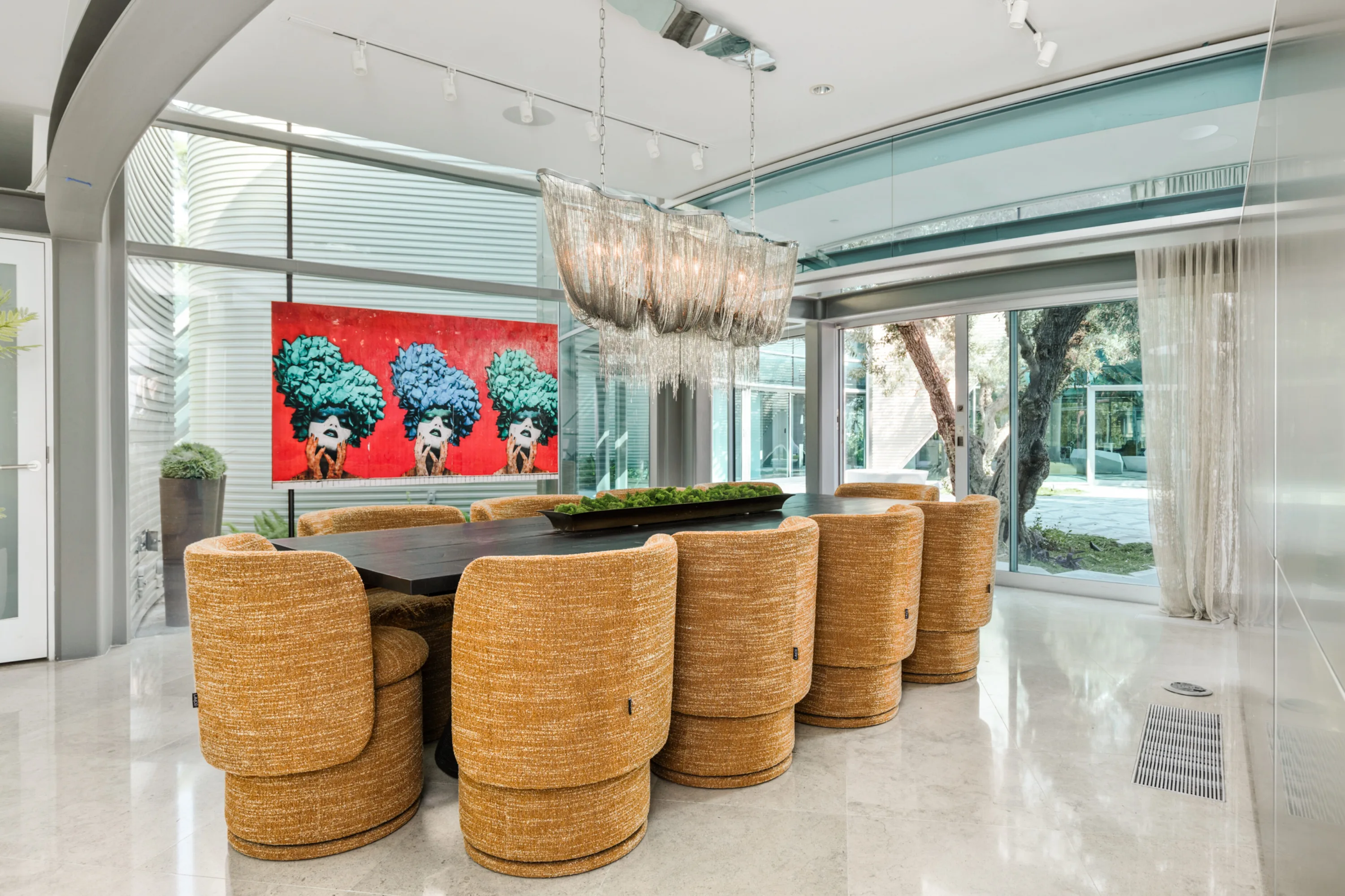 Dining room seating ten in round bouclé chairs beneath a fringed chandelier, bold red pop-art canvas behind