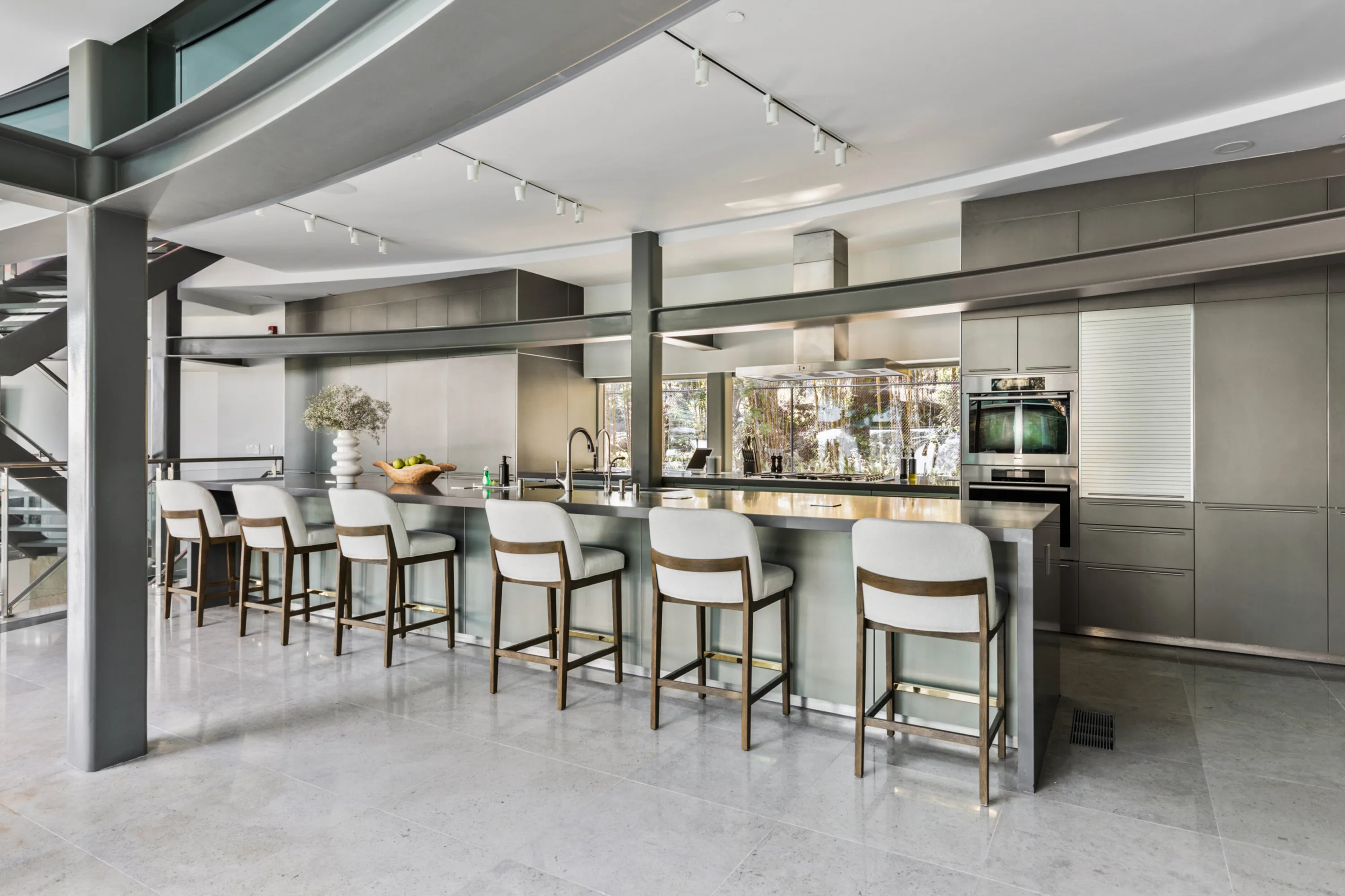 Chef's kitchen in brushed steel with a six-stool breakfast bar, double ovens and curved steel beams overhead