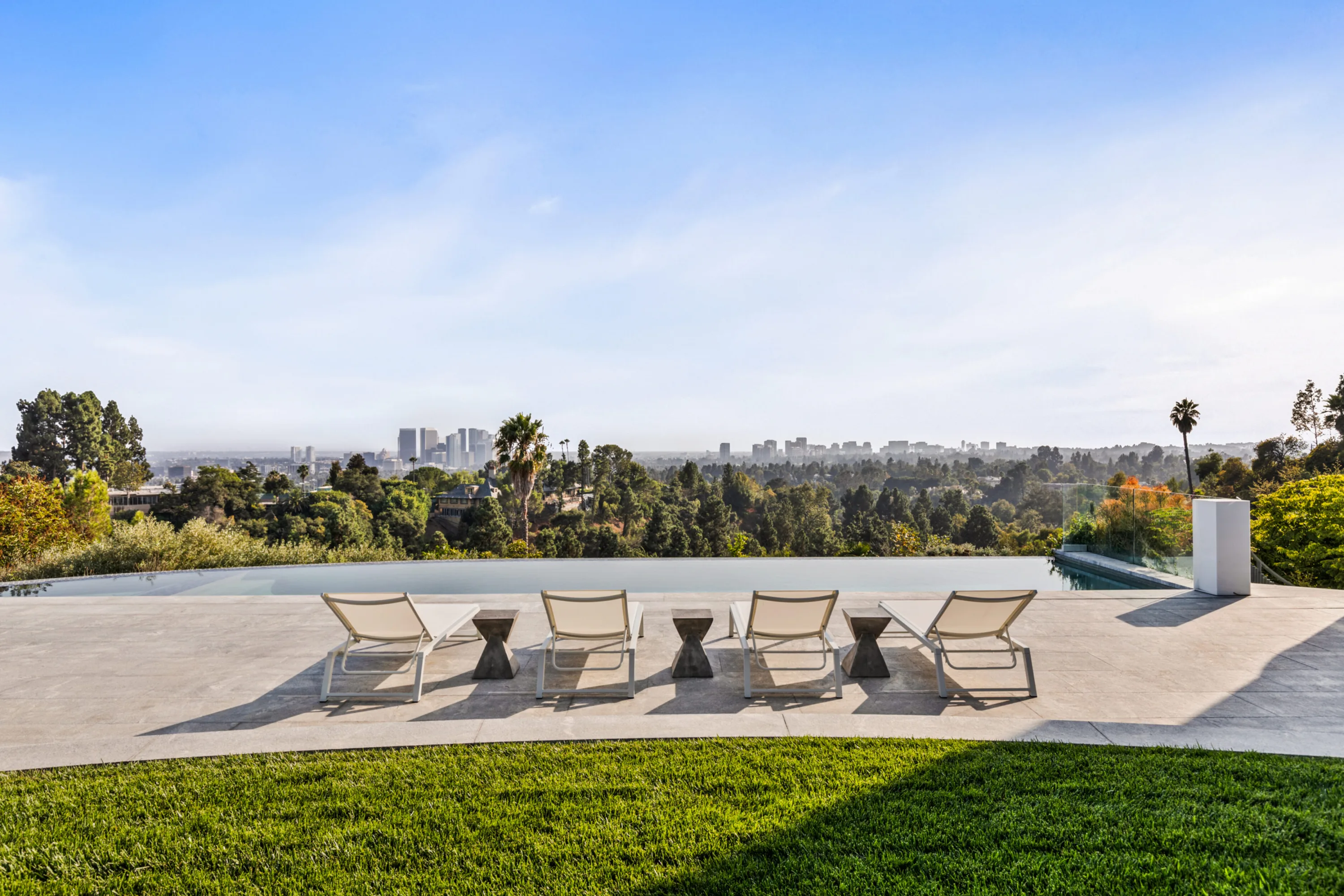 Infinity pool edge dissolving into treetops with the Century City skyline beyond, four loungers on the deck