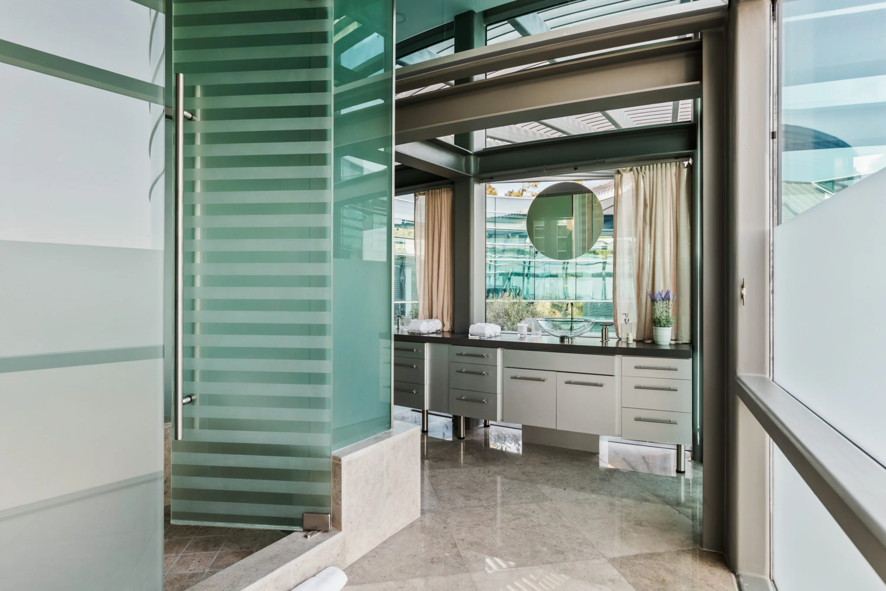 Ensuite entry through a fluted glass shower screen to a long vanity with round mirror and garden outlook