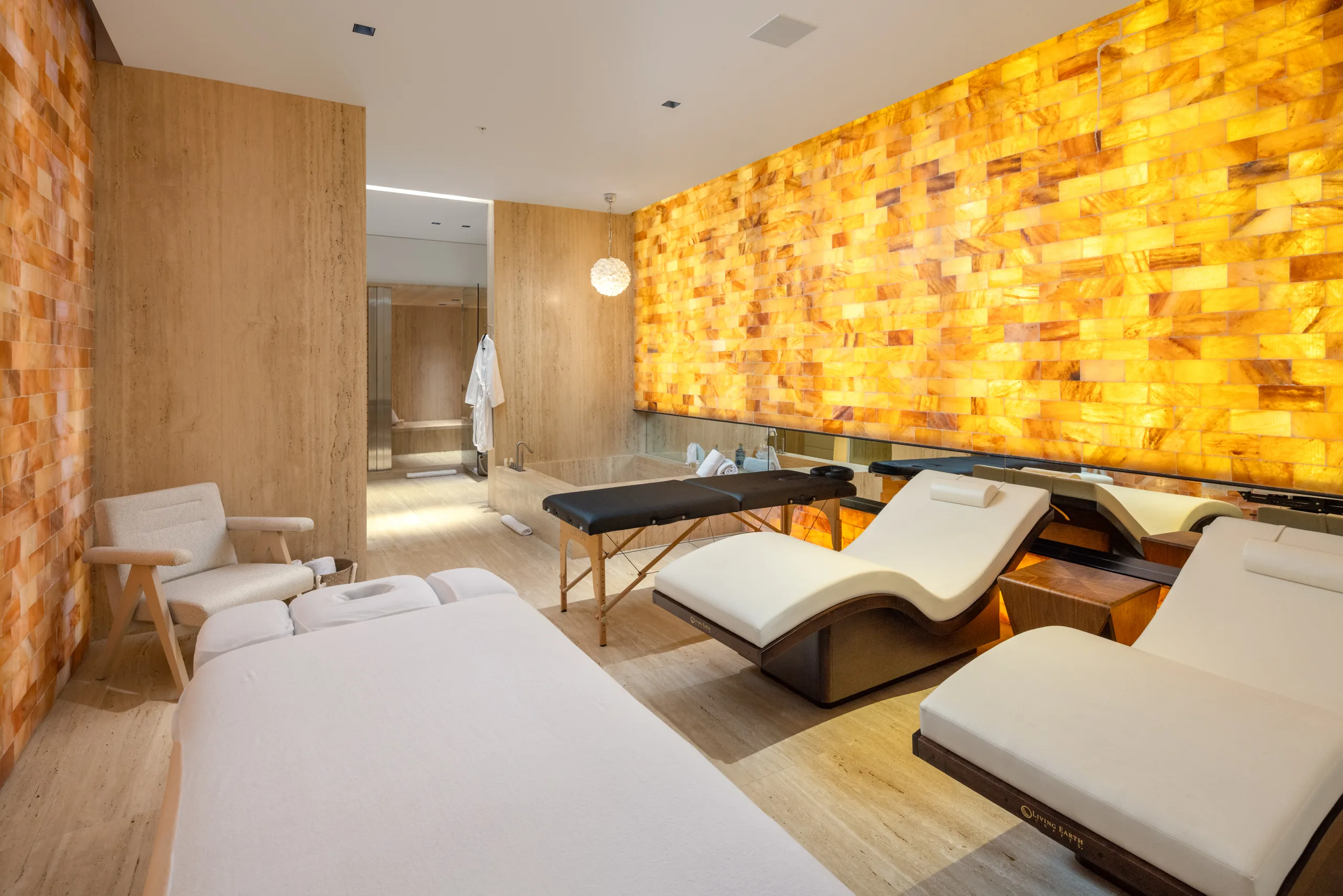 Spa treatment room with twin massage tables, relaxation loungers and a backlit salt-brick wall