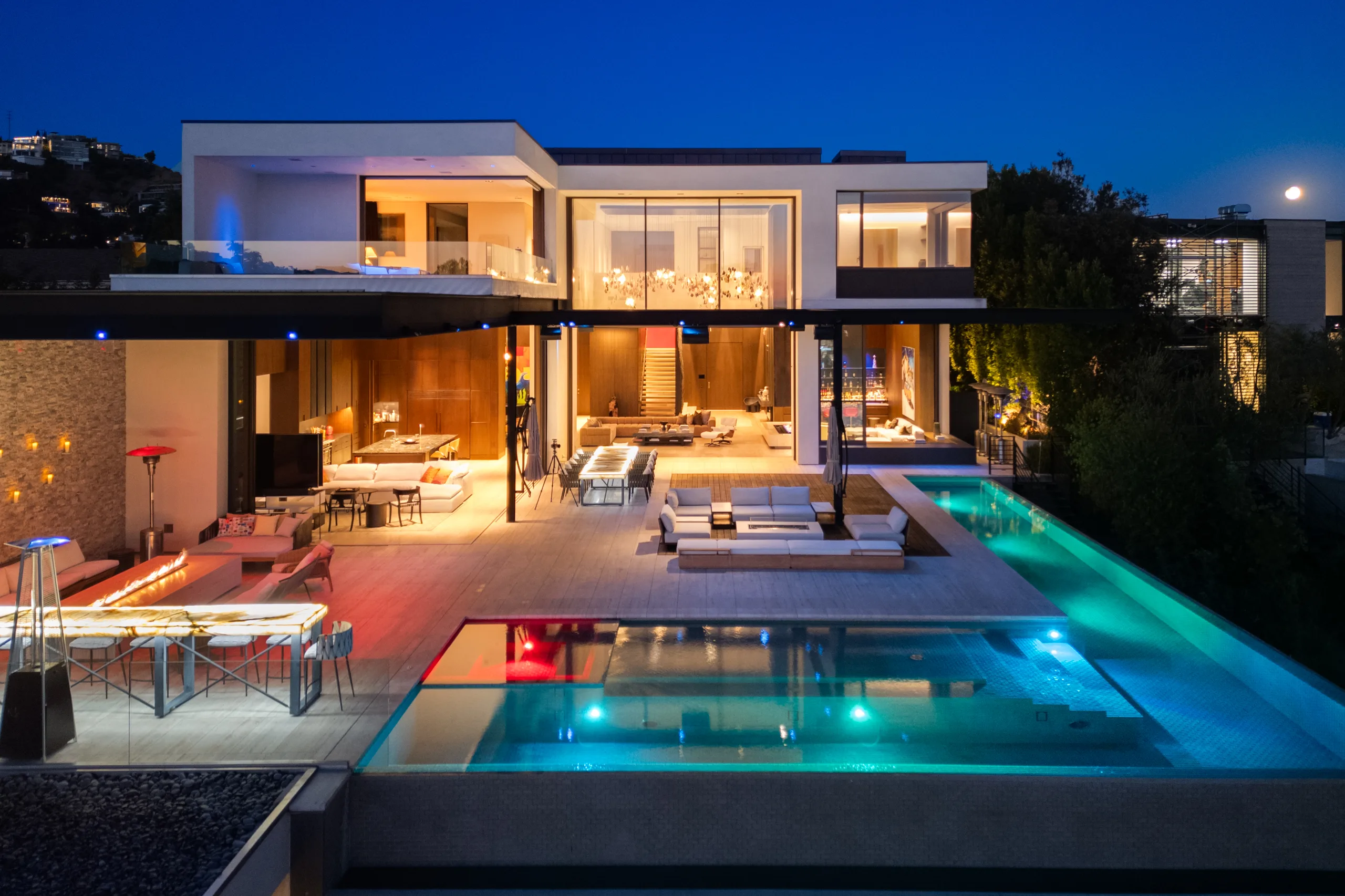 Rear elevation at nightfall, lit pool and spa below open living pavilions and a fire-table terrace