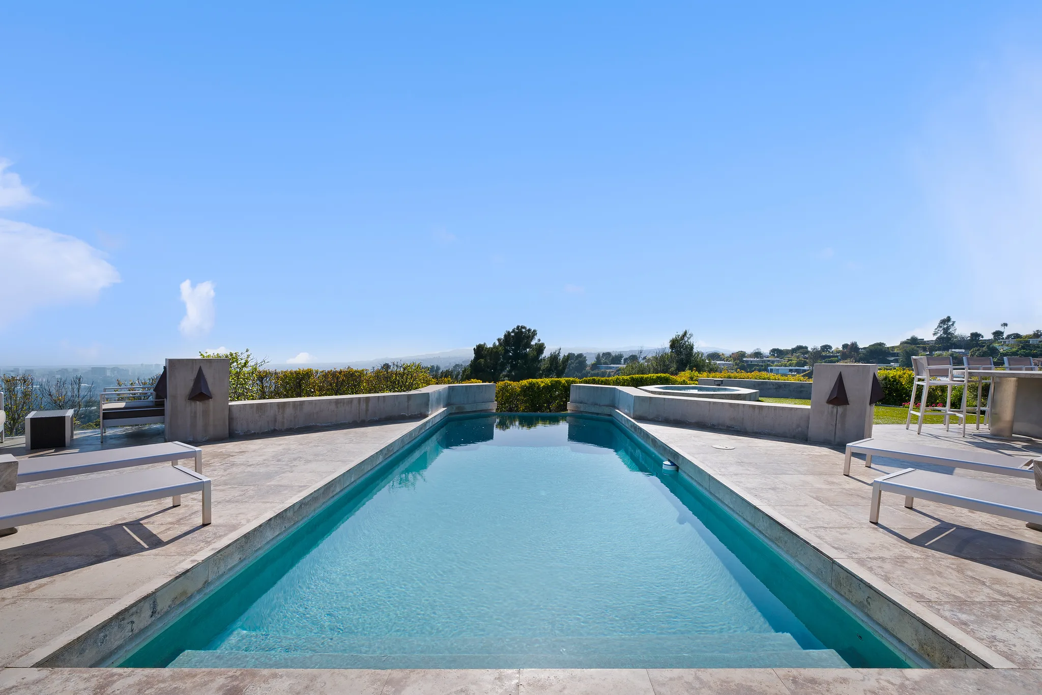 Lap pool in travertine decking with sun loungers, spa and treetop horizon beyond