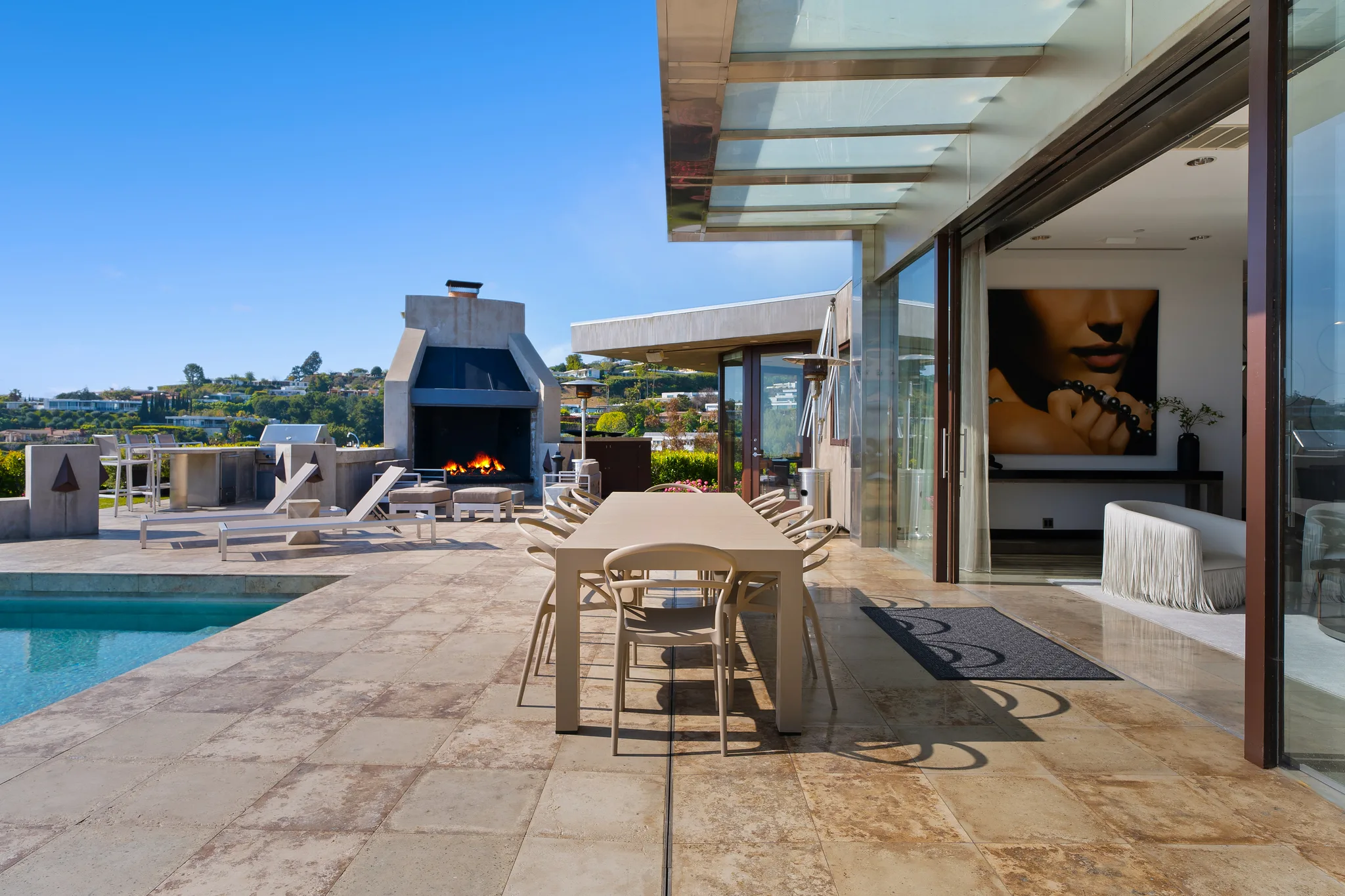 Poolside terrace with long dining table under a glass canopy and an outdoor fireplace alight