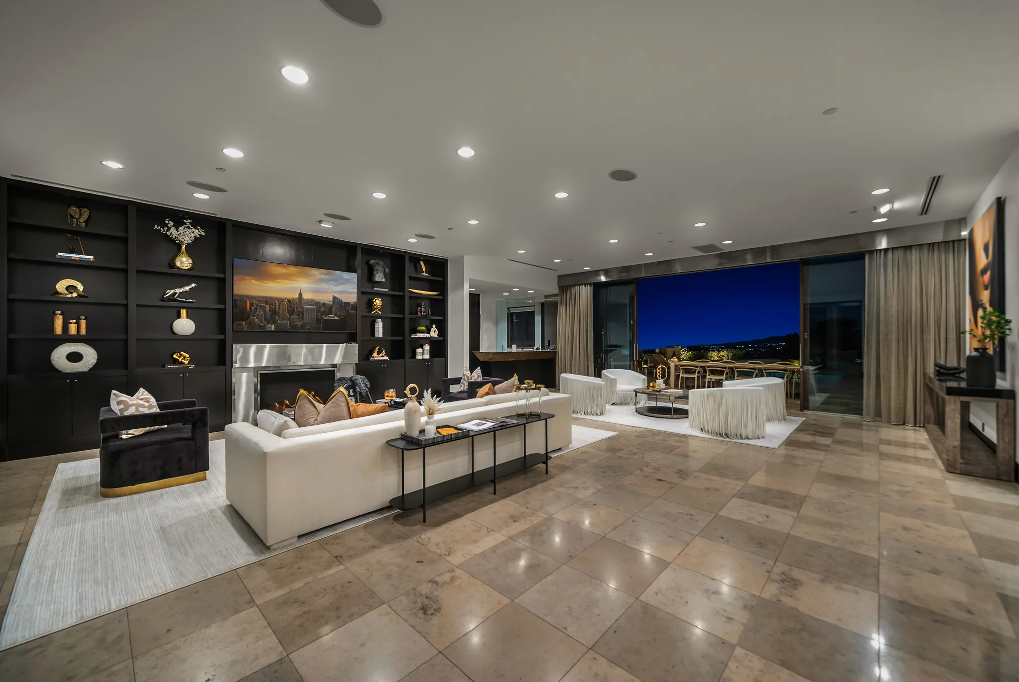 Open-plan living room with white sectional, black built-in shelving and sliding walls onto a terrace at nightfall