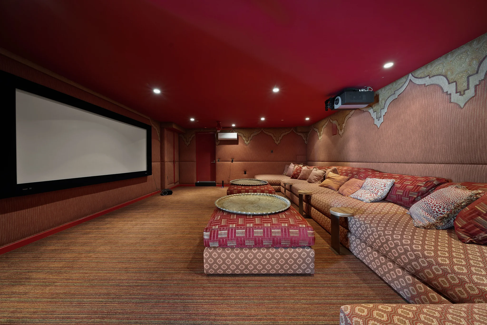 Screening room with wide projection screen, deep patterned banquette seating and red ceiling