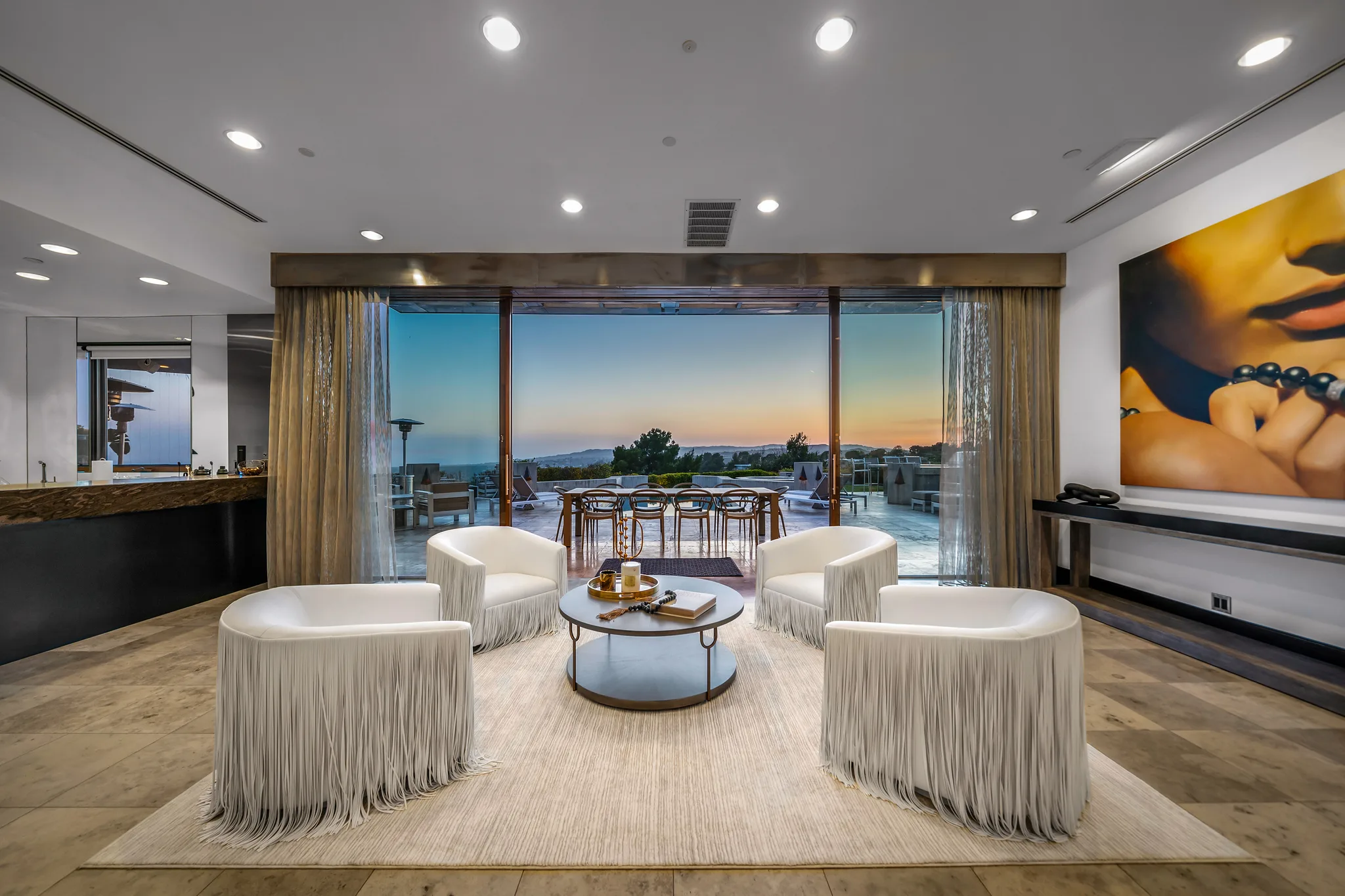 Conversation lounge of four fringed armchairs facing sliding doors and a sunset over the city