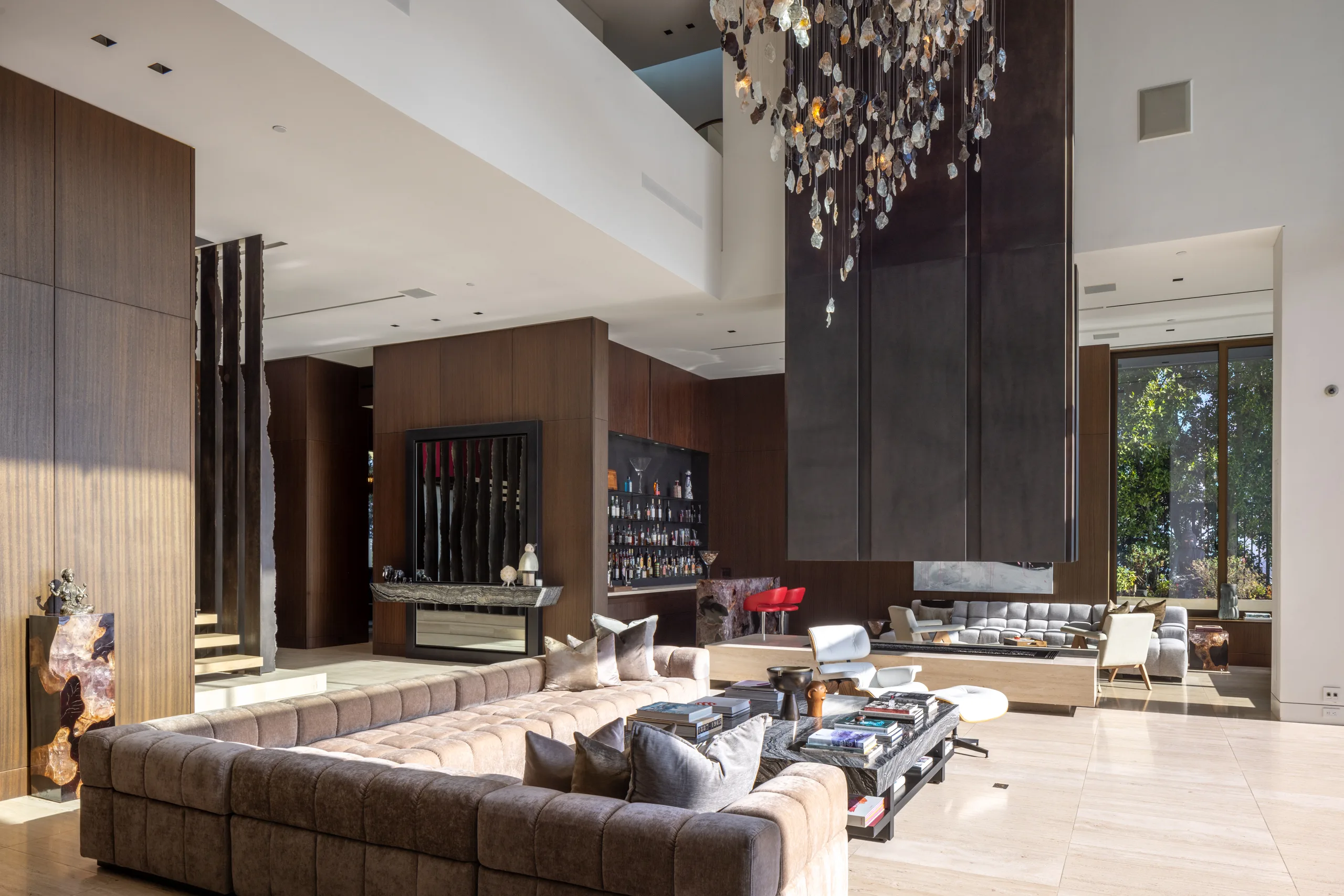 Double-height great room with tufted sectional, stone fireplace, back bar and cascading quartz chandelier