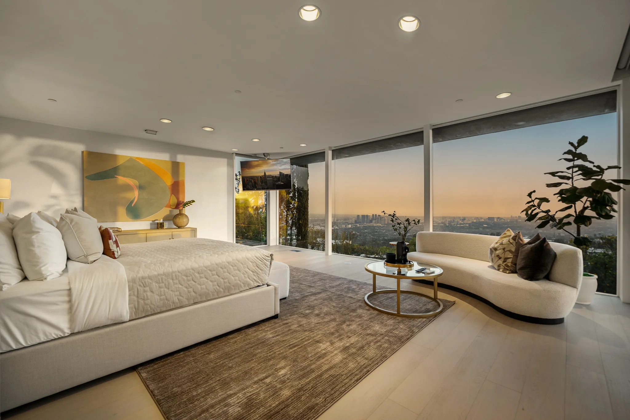 Primary suite with curved sofa and floor-to-ceiling glass framing the skyline at golden hour
