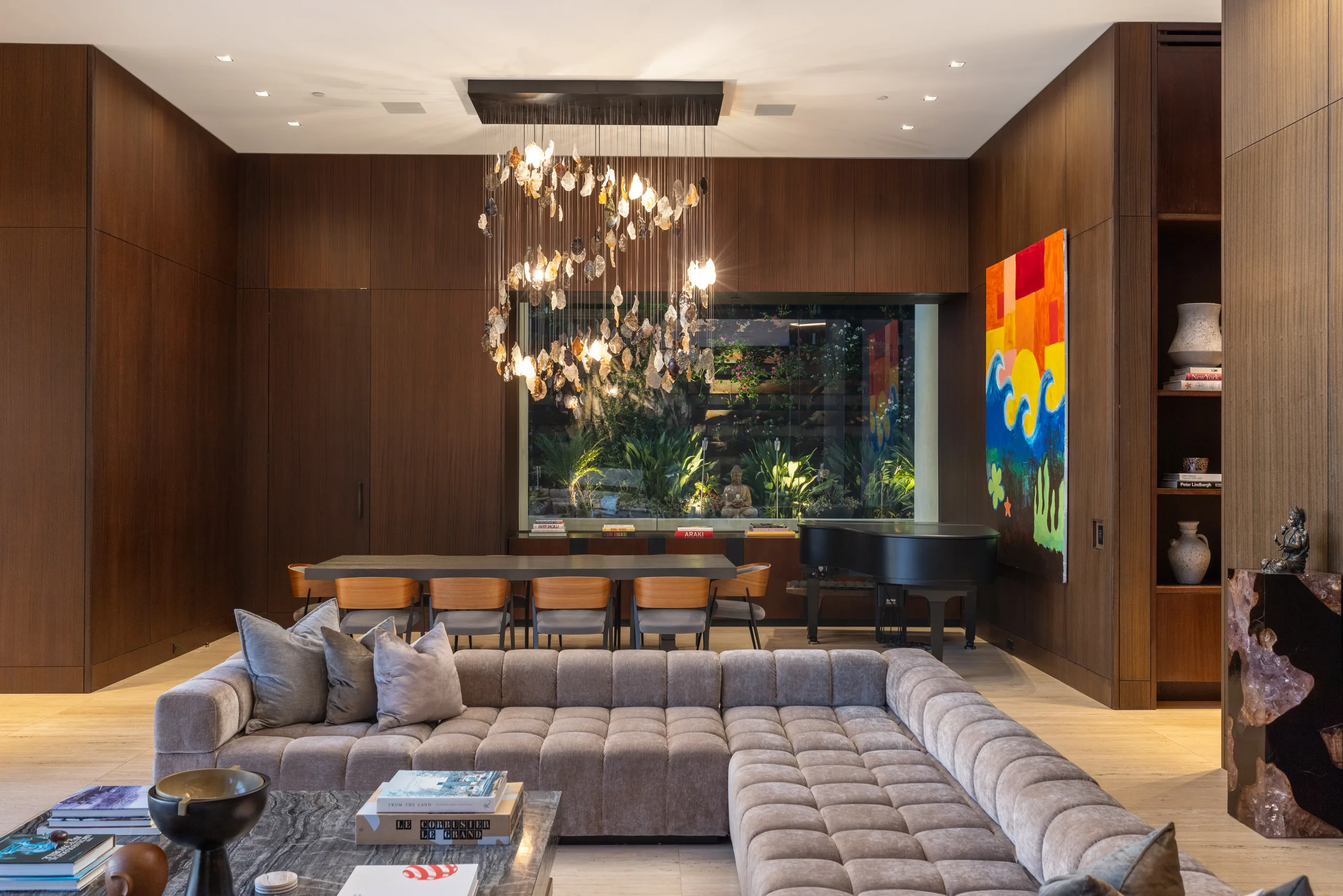 Walnut-panelled lounge and dining table beside a grand piano, with a planted atrium window behind