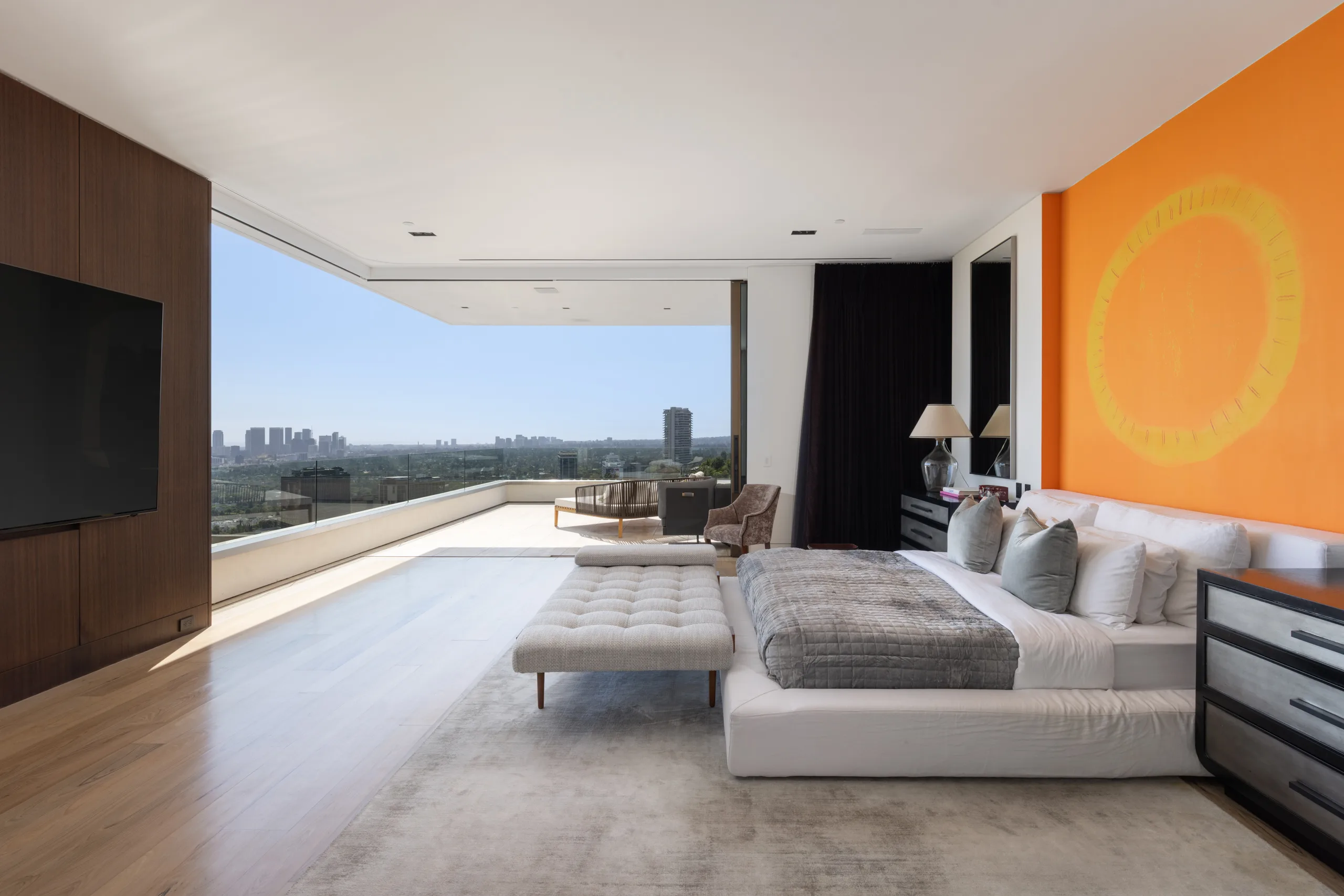 Primary suite with sliding glass wall opening to a terrace above the city and a sun-motif orange feature wall