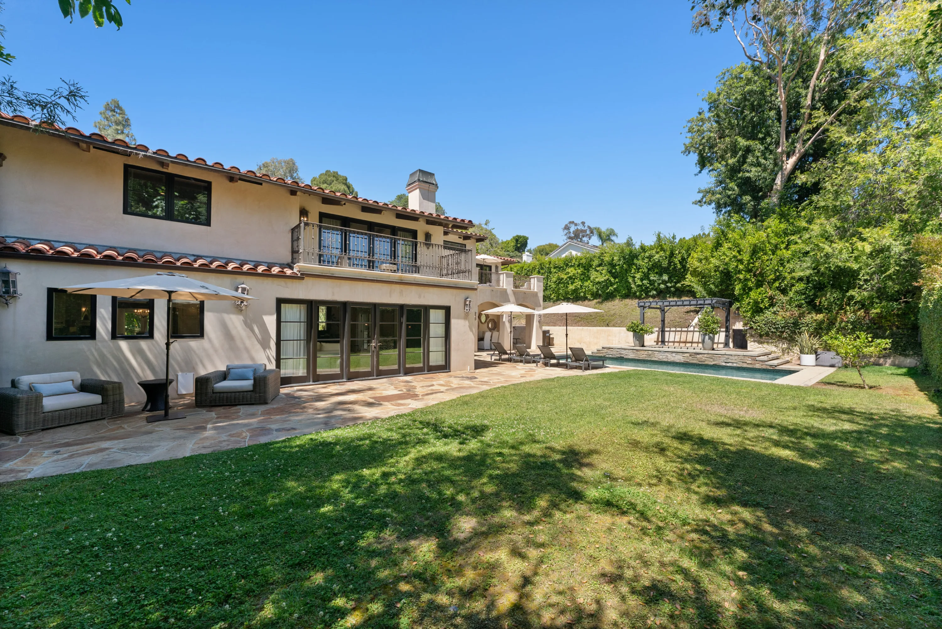 Level lawn and flagstone patio wrapping the tiled-roof house, with the pool beyond