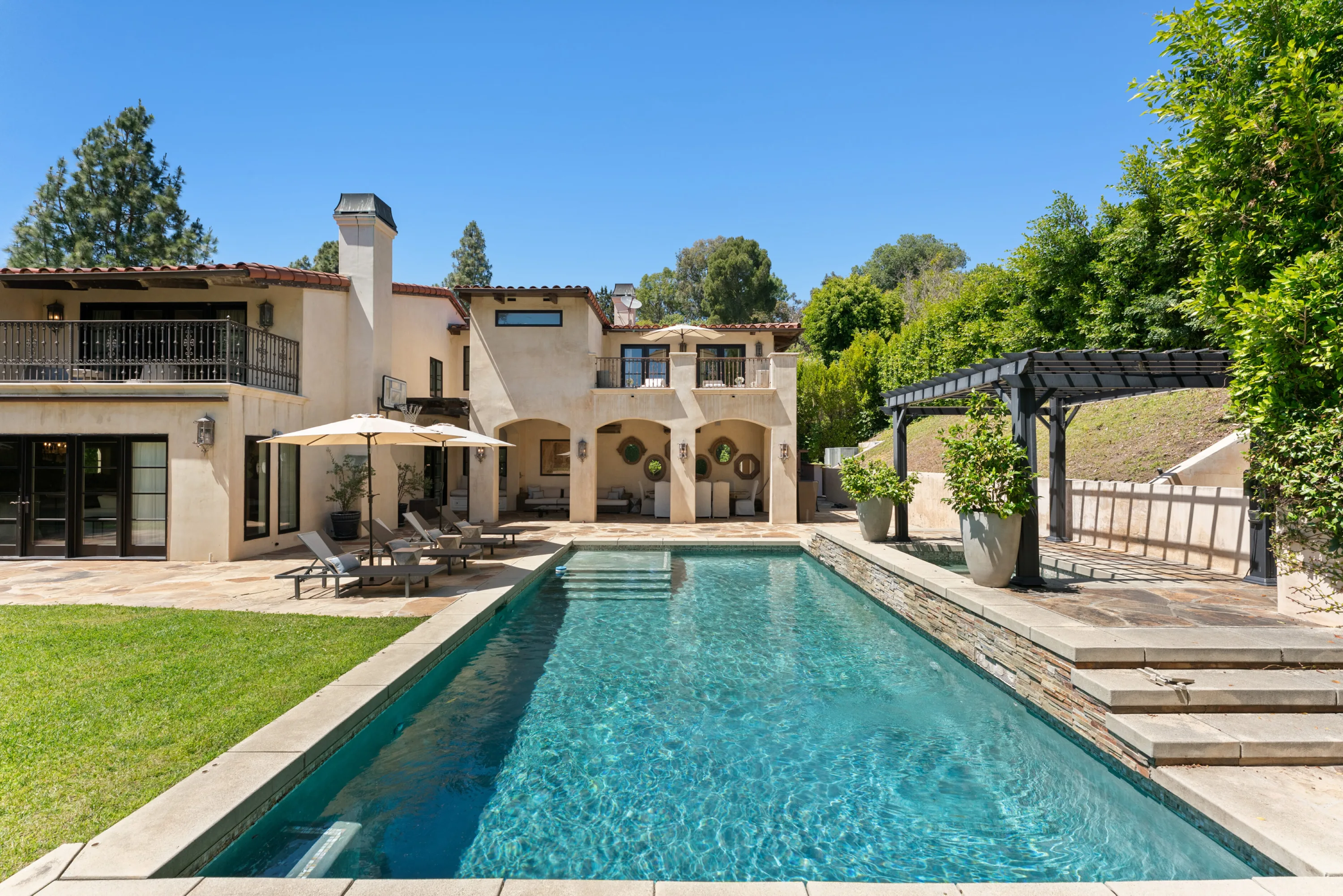 Long rectangular pool stretching toward the arcaded rear terrace and upper balcony of the villa