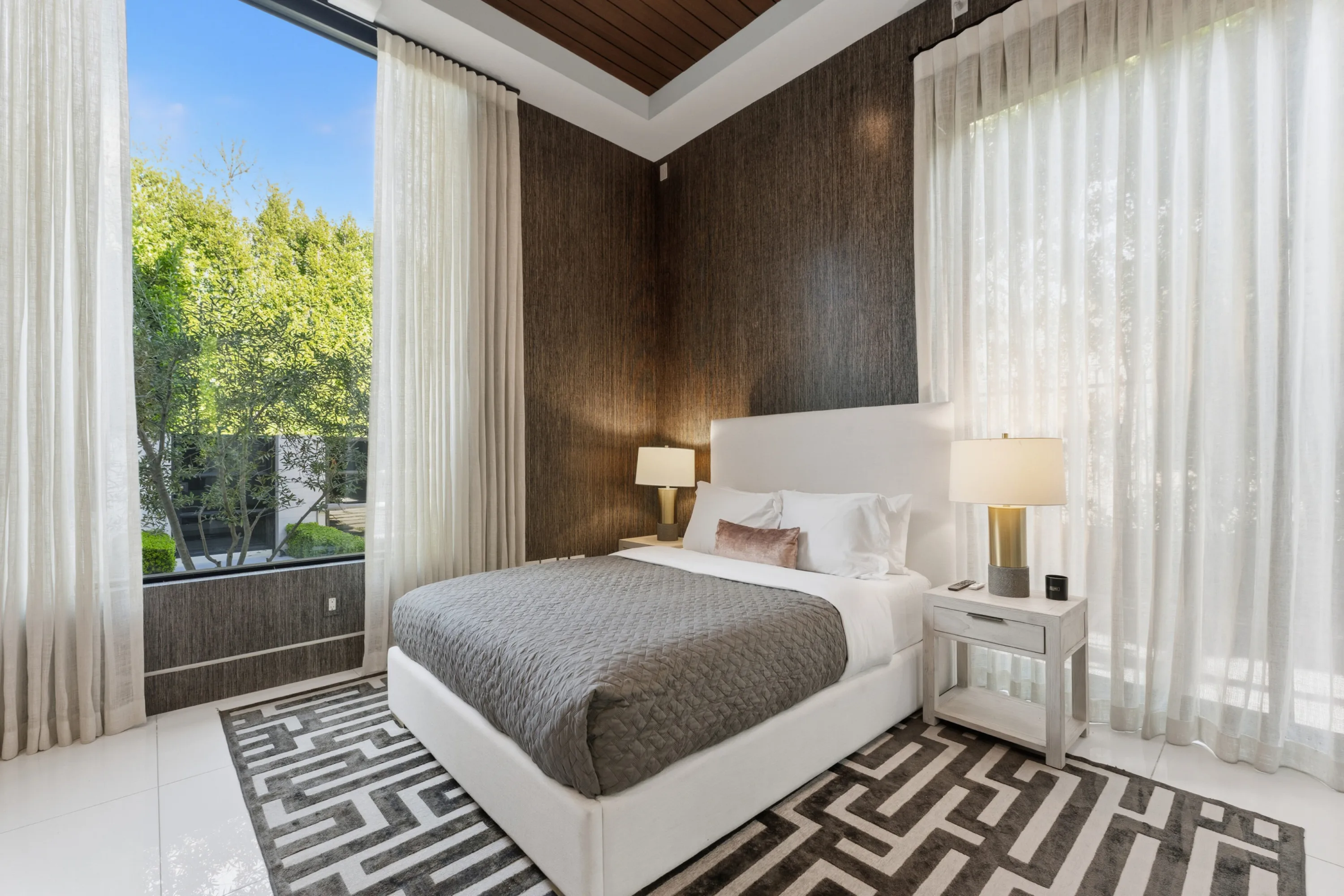 Corner guest room with sheer-curtained floor-to-ceiling glass, grasscloth wall and treetop greenery outside