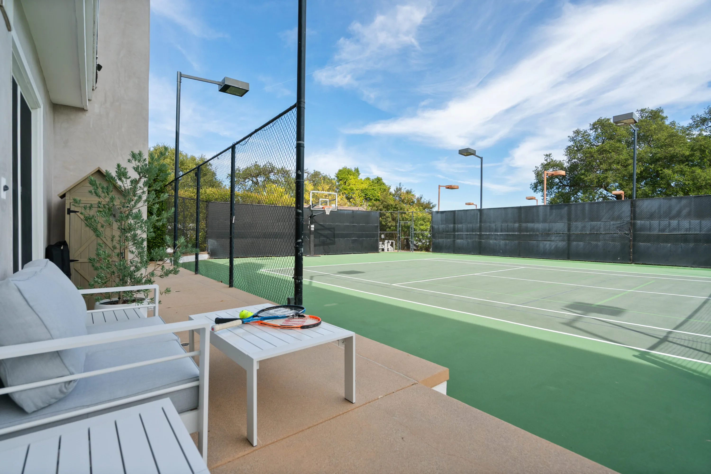 Courtside seating nook with rackets and ball on a low table, looking across the green hard court